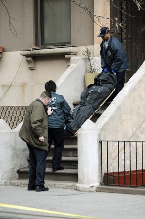 Two police officers and a man are standing on a sidewalk near a staircase, inspecting large black bags.