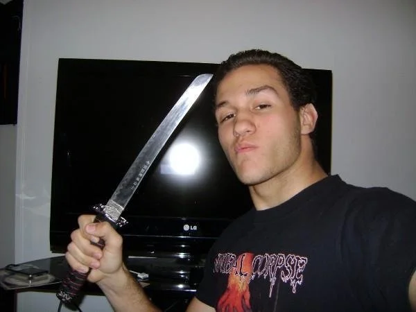 A young man holding a large sword, making a serious expression, standing in front of a black television.