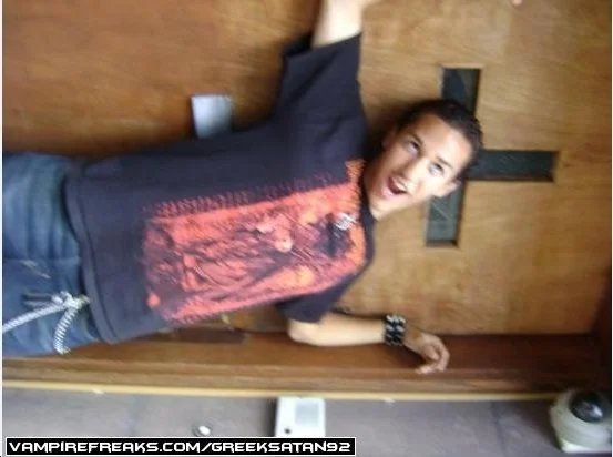 Person standing in front of a wooden wall with a cross, smiling and looking at the camera.