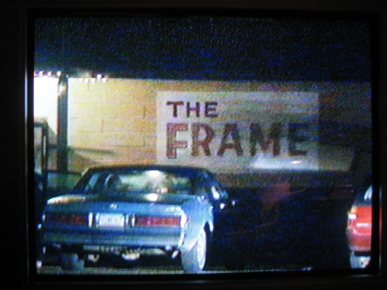 A sign that reads 'THE FRAM' in a parking lot at night.