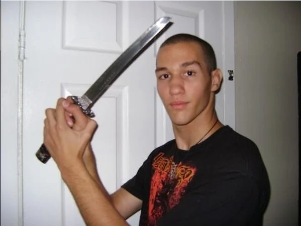 Young man with short hair holding a sword in a room with white door