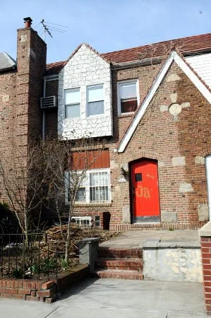 A brick house with a red door, white trim, and a small garden in front, under a clear blue sky.