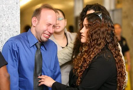 A woman comfortingly touches a man who appears to be crying in a public indoor setting.