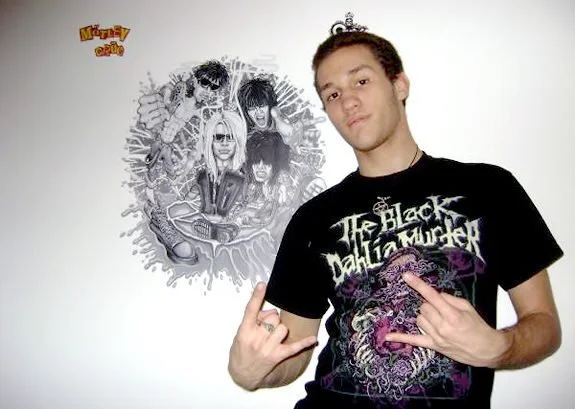 Young man making a rock sign with his hand in front of a wall with a black and white mural of The Black Dahlia Murder band members.