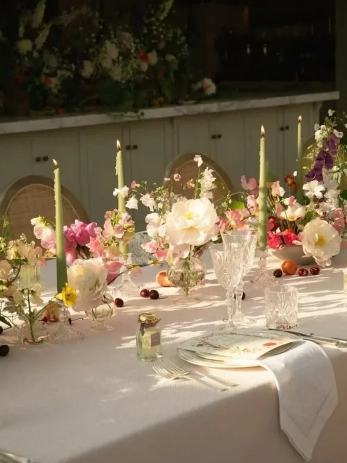 Elegant table set for a formal event with floral centerpieces, lit candles, and fine china, decorated with scattered berries and fruit.