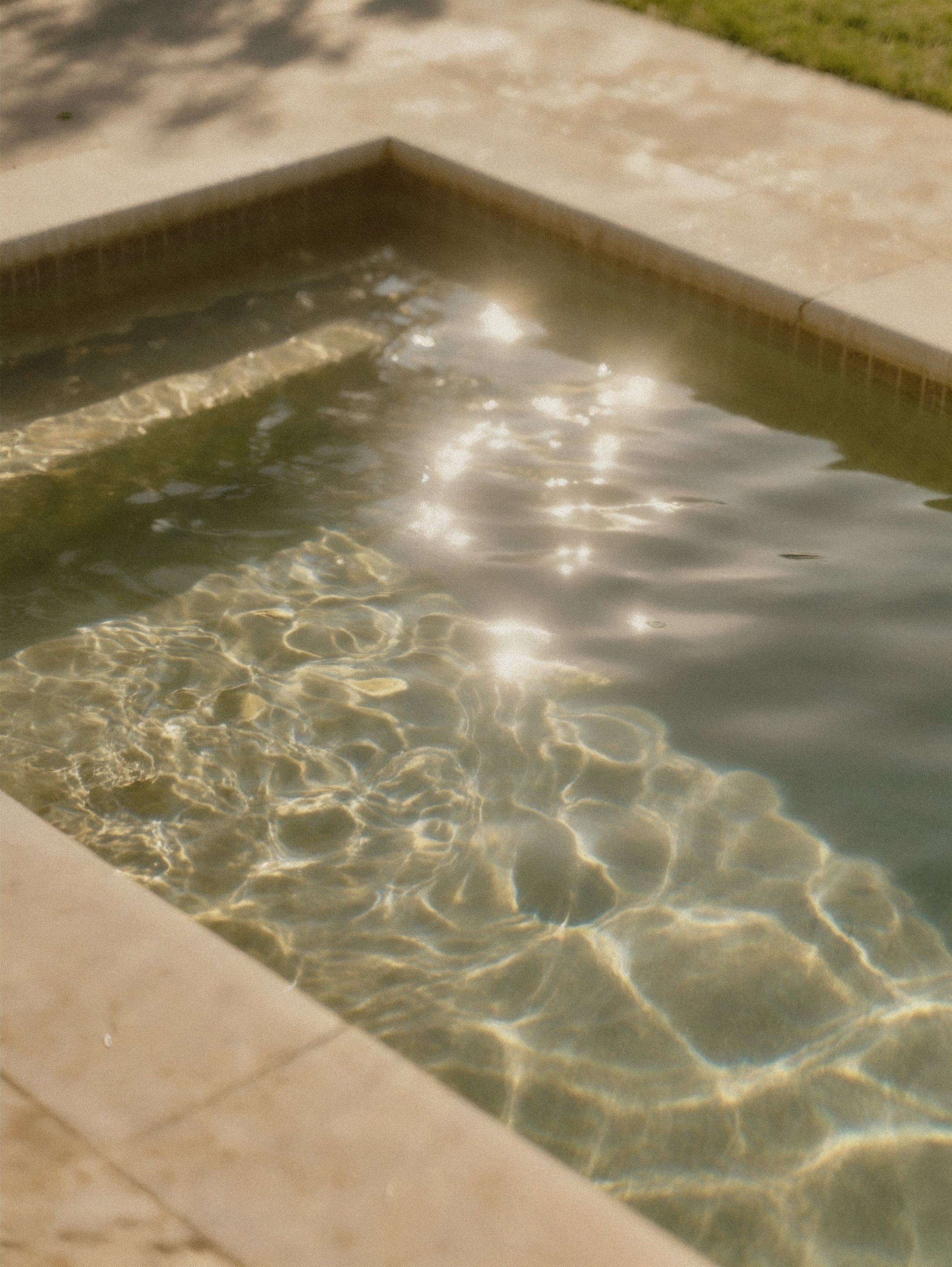 A close-up of a small rectangular outdoor pool with clear, slightly rippling water, and sunlight reflecting on the surface.