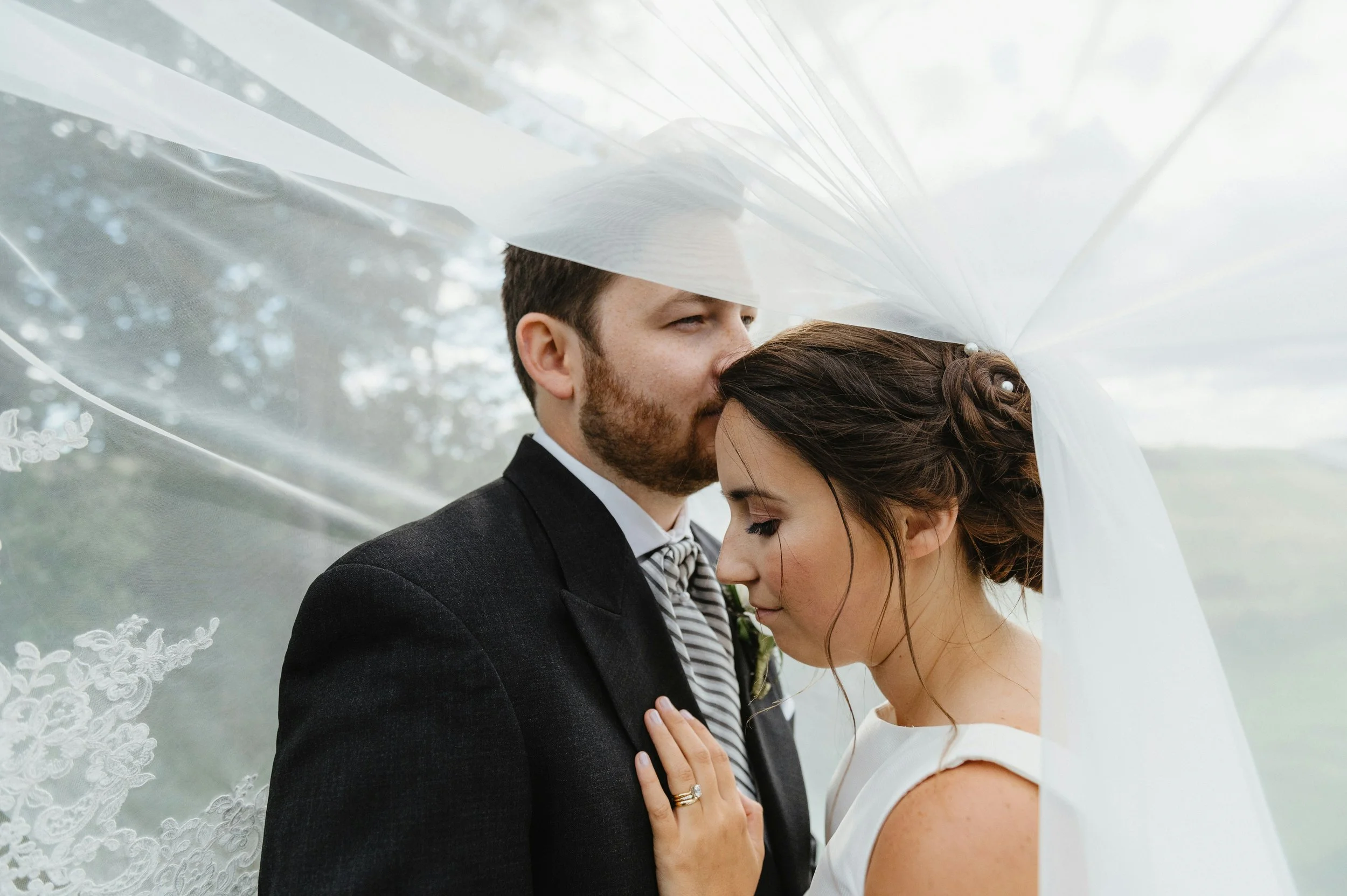 Bride and groom standing close together under a wedding veil with their eyes closed and foreheads touching during their wedding.