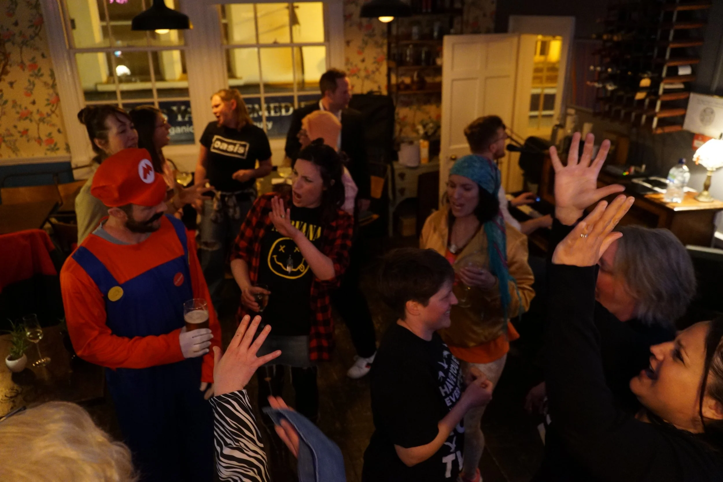 Group of people at a lively indoor party, some dancing and engaging in conversation, with colorful lighting and a warm, cozy atmosphere.