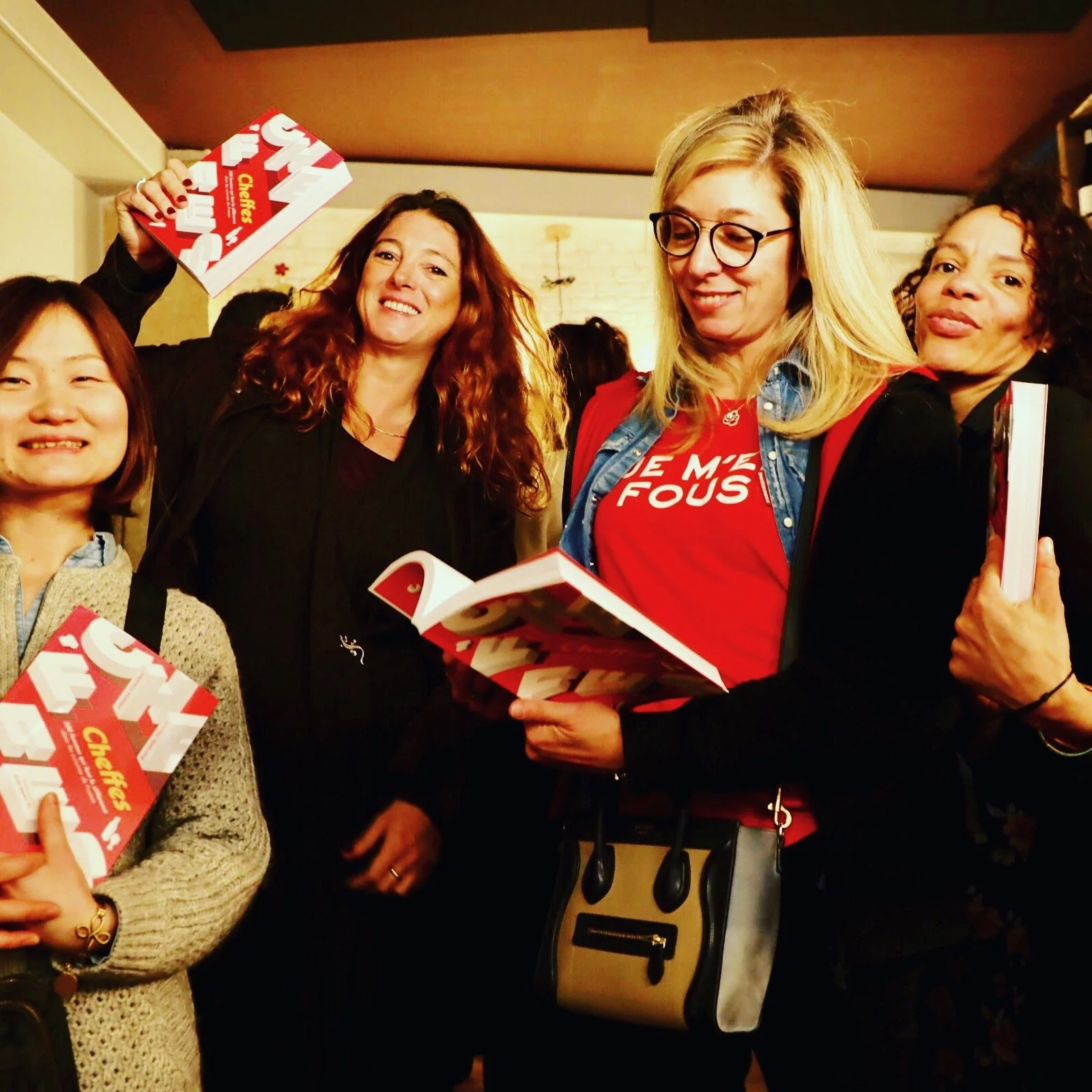 A group of female journalists, chefs and food entrepreneurs gathered together, holding the book CHEFFES, at an indoor event.