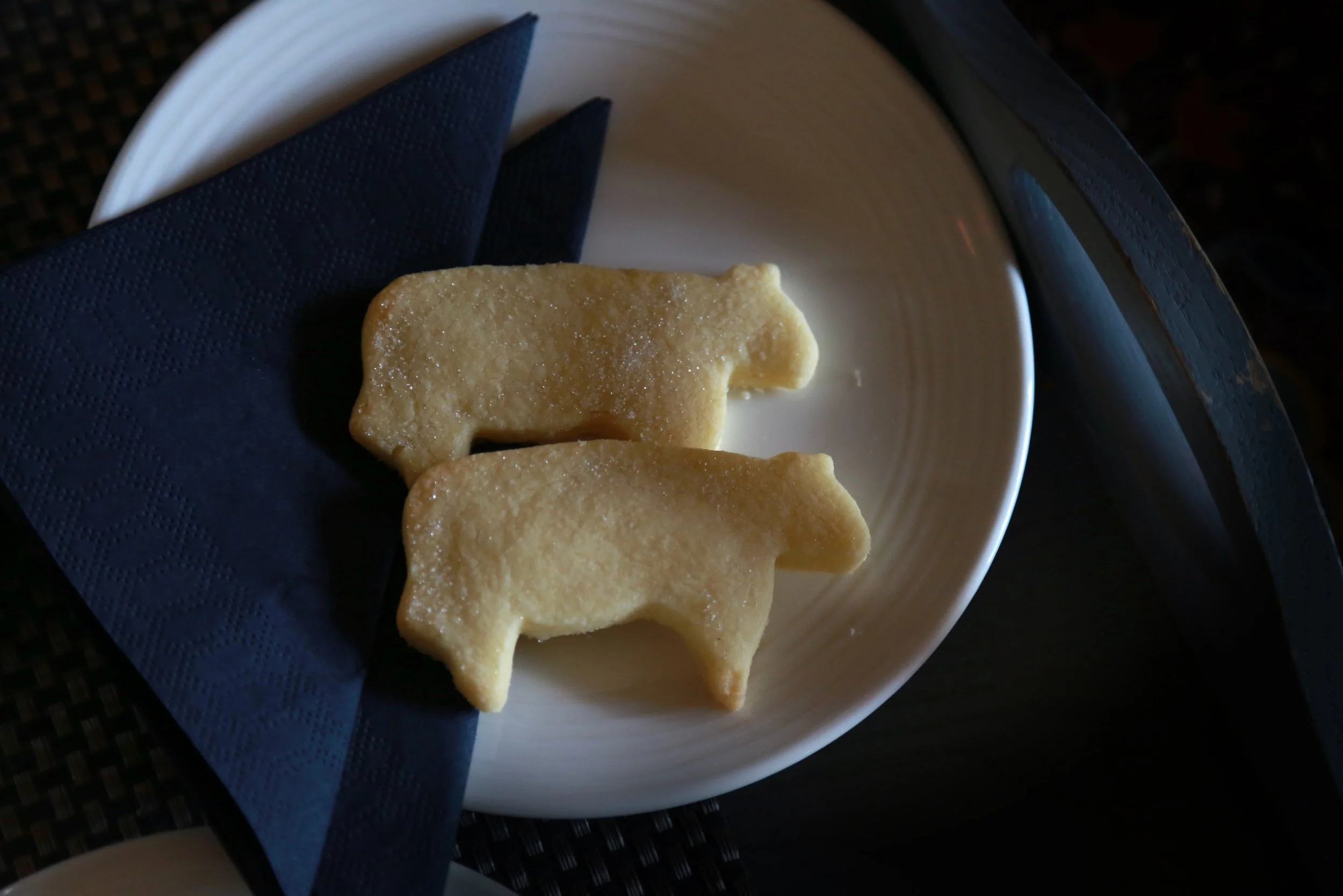 Two sugar cookies shaped like pigs on a small dish with a blue napkin. Taken from the book "STEAK IN FRANCE".