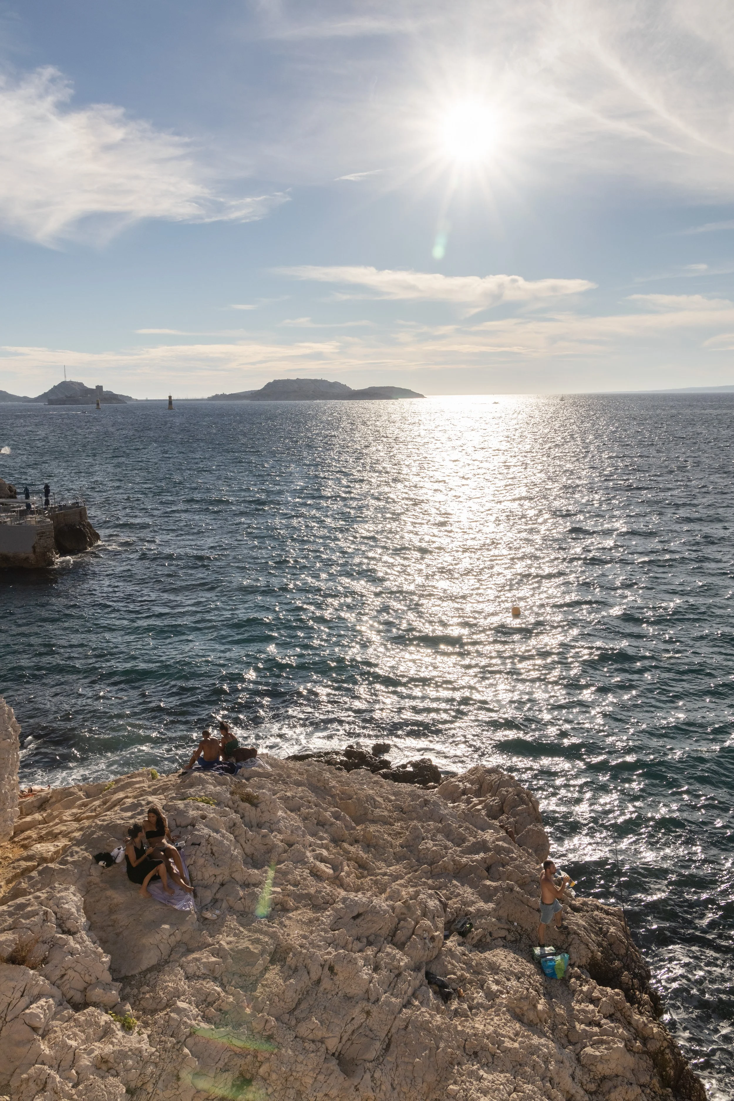 People in Marseille sitting on the rocky coast enjoying the sunset over the Mediterranean Sea.