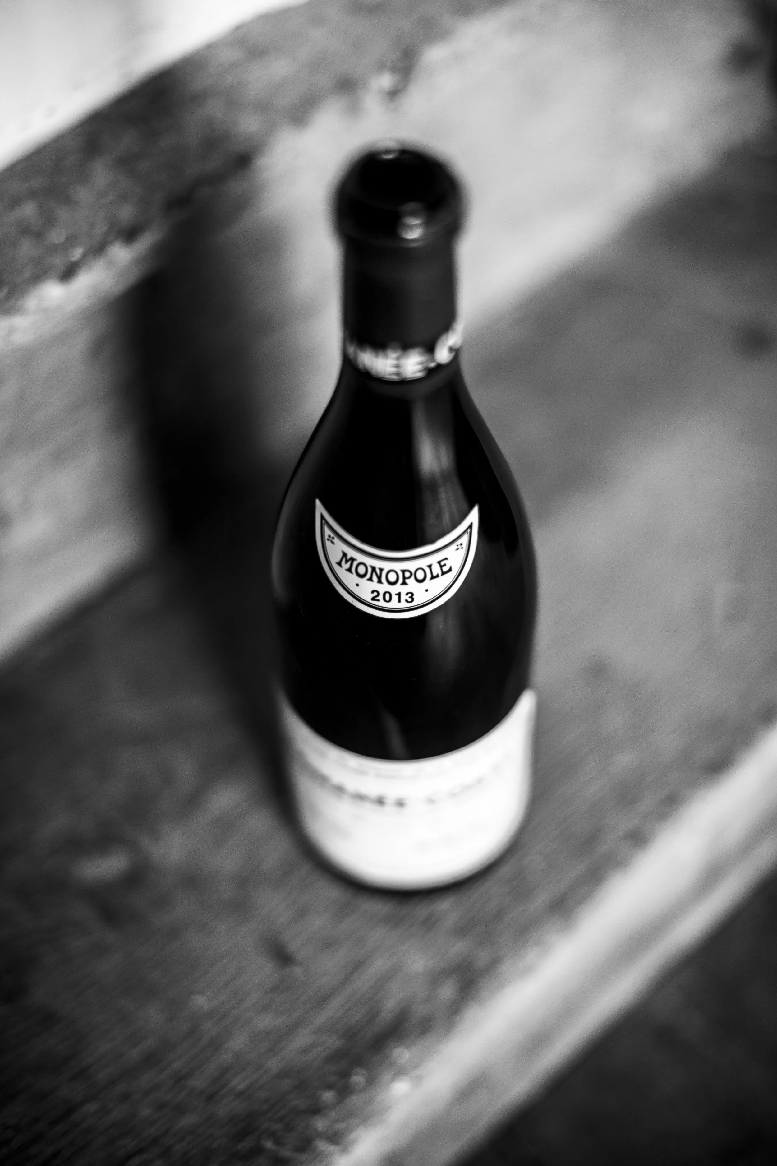 A black and white photo of a bottle of Romanée Conti, labeled 'Monopole 2013' on a wooden surface, photographed by Vérane Frediani.