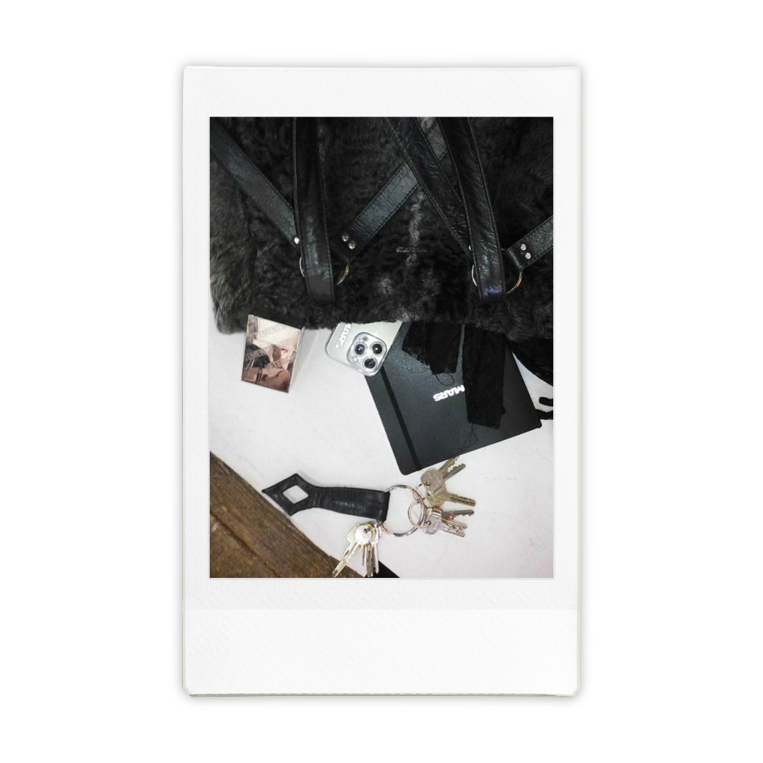 Items on a table including a black handbag with straps, a mobile phone, a black box or notebook, a set of keys with a leather keychain, and a small rectangular object.