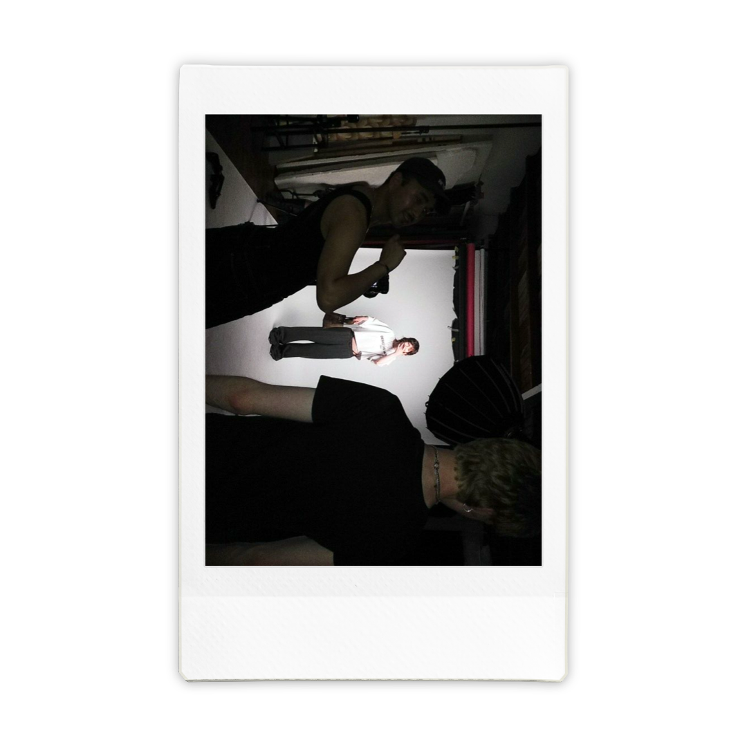 People behind the scenes at a photography studio, with one person in the foreground and a model on a white backdrop in the background.