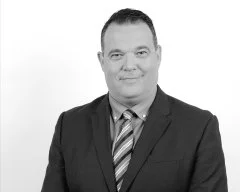 Black and white photo of a man in a suit with a striped tie, smiling at the camera.