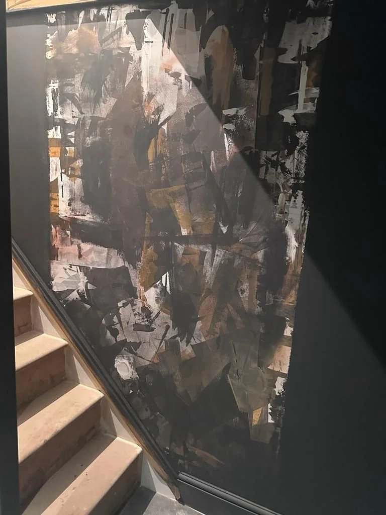 Abstract modern art mural with dark and earthy tones next to a staircase.