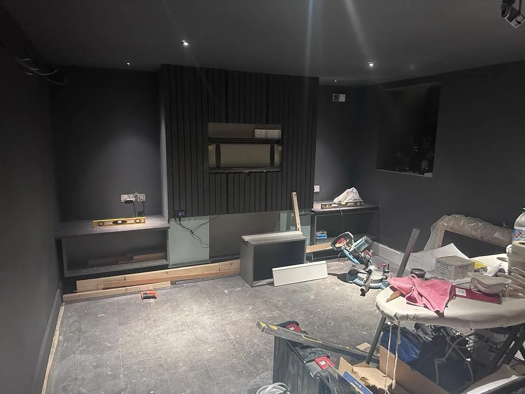 Under construction room with black walls, some tools, materials, and an unfinished TV or fireplace wall in progress.