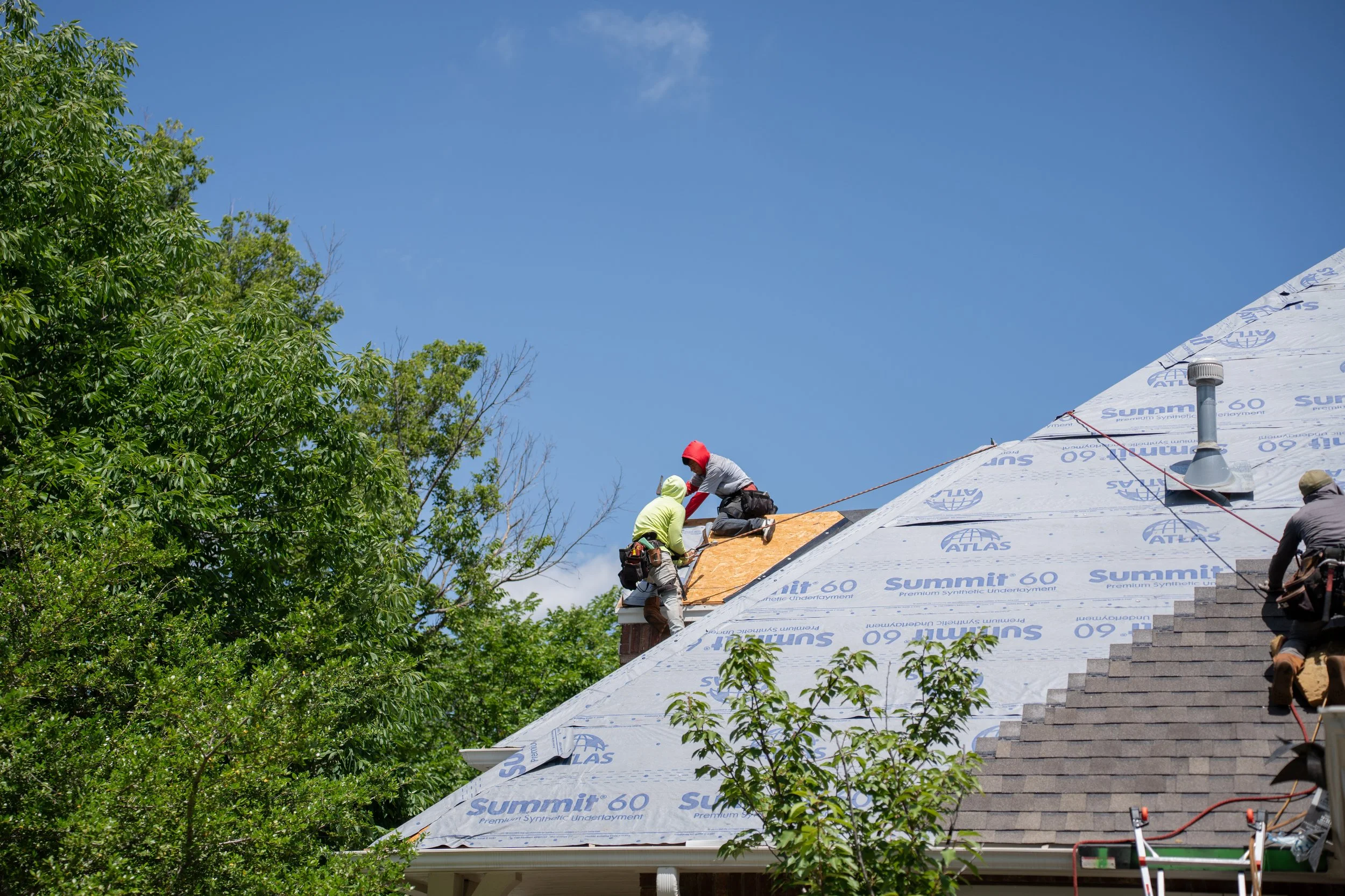 Three people working to replace a roof with new shingles and gutters after a storm