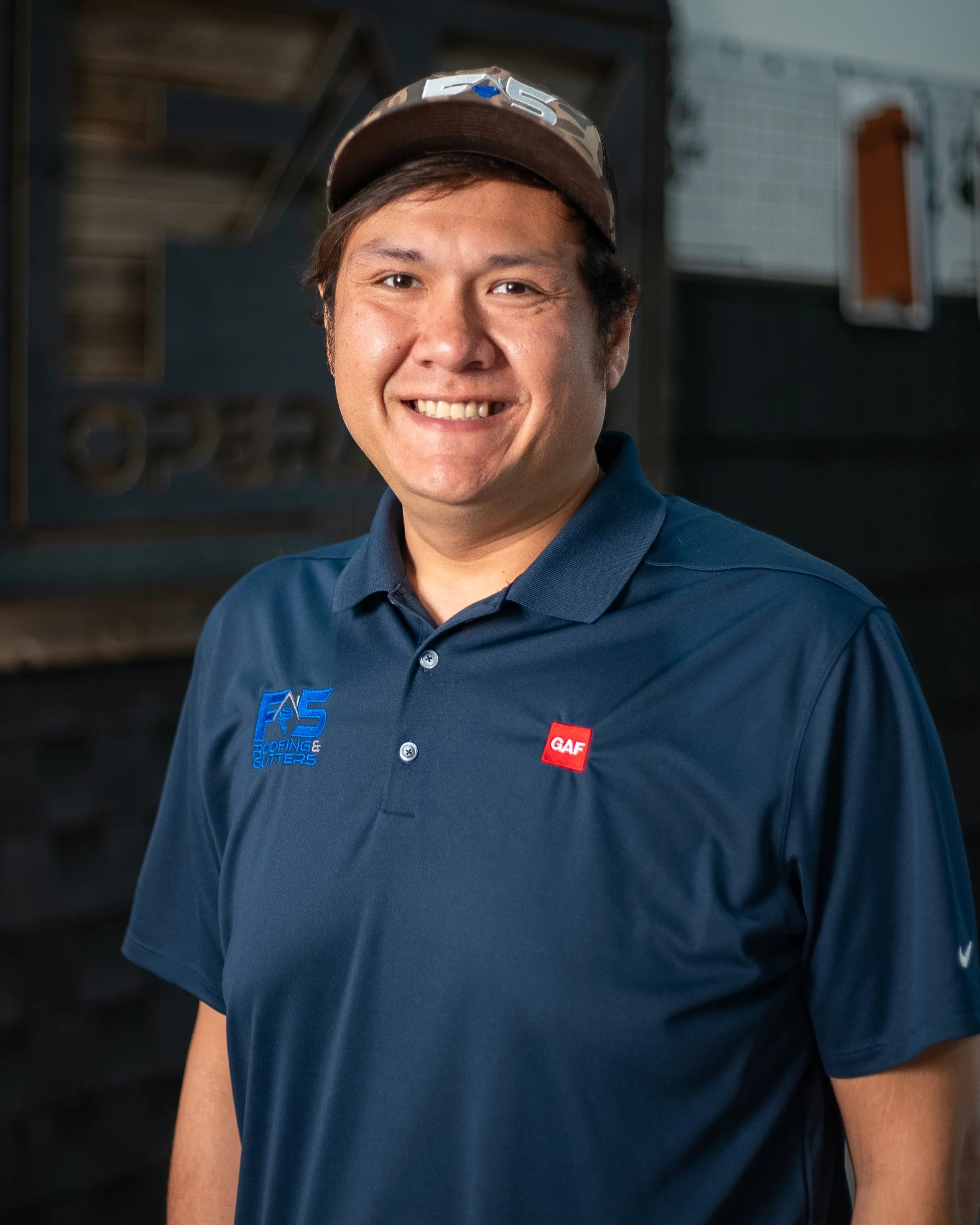 Man smiling at camera wearing a ball cap with a navy polo on