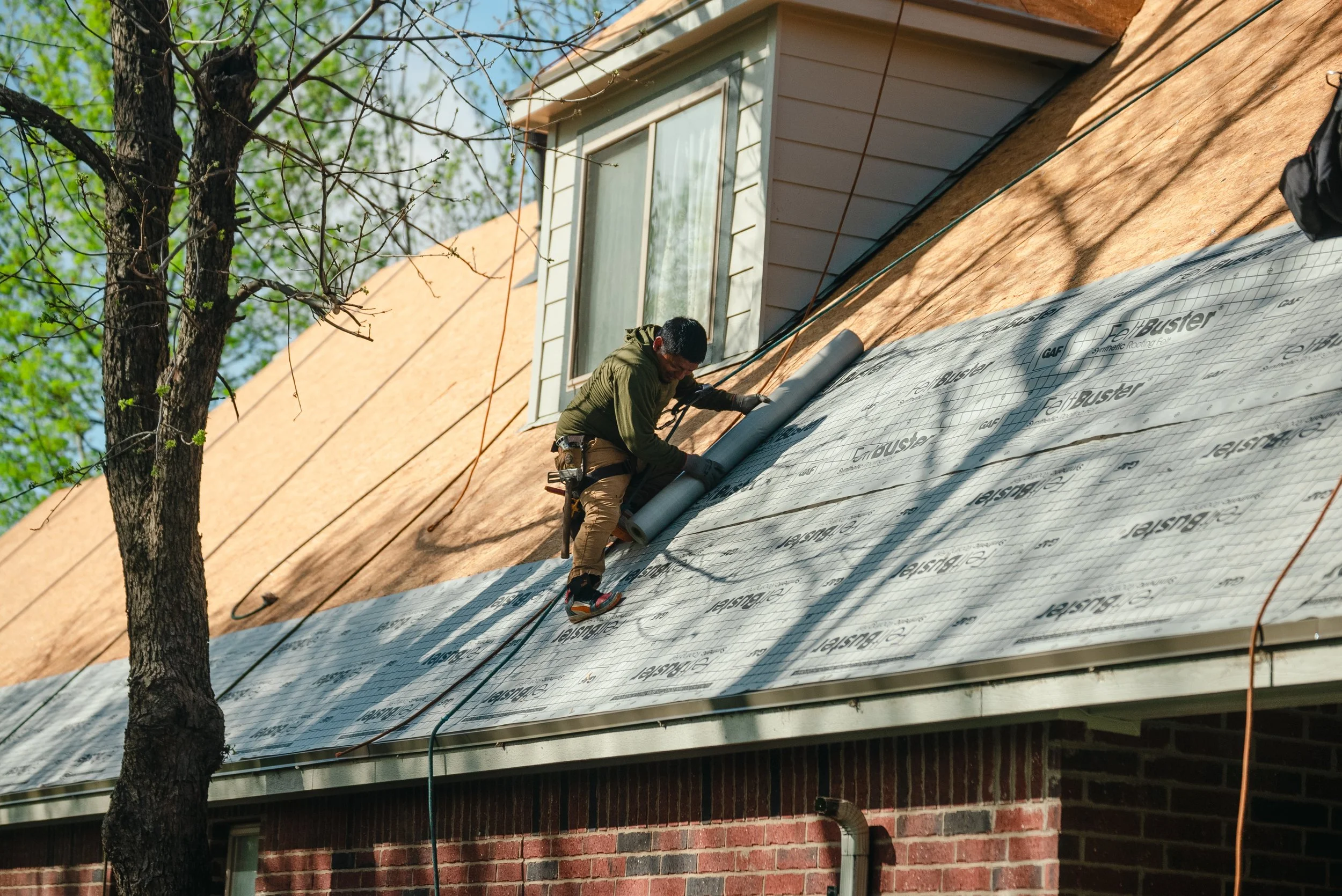 A man in a green sweatshirt and tan pants working on a full roof replacement in Bartlesville, Oklahoma