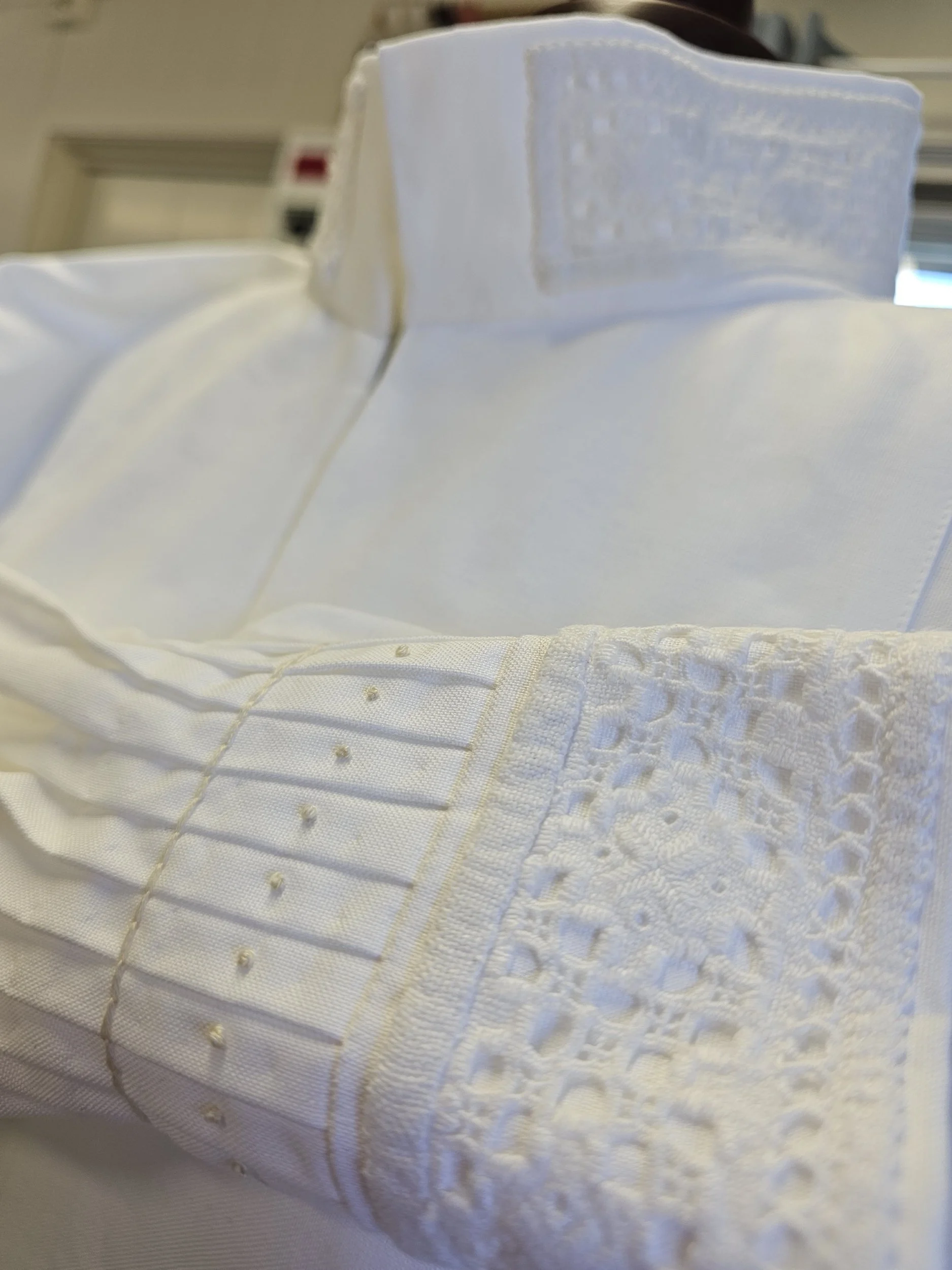 Nærbilde av en hvit brodert sengeteppe med lukkede hjerter og geometriske mønstre.