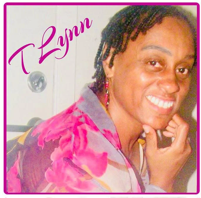 A woman with short dreadlocks, smiling and resting her chin on her hand, wearing a colorful shirt. The name 'T Lynn' is written in purple cursive font in the top left corner.