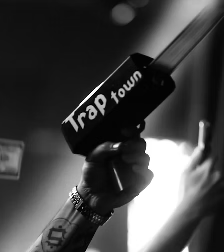 Mano con tatuaggi e braccialetto che tiene un microfono con la scritta 'Trap tour', sfondo oscuro e luce brillante