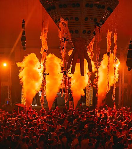 Evento musicale con grande folla, fuochi artificiali, e un palco con performance artistica.