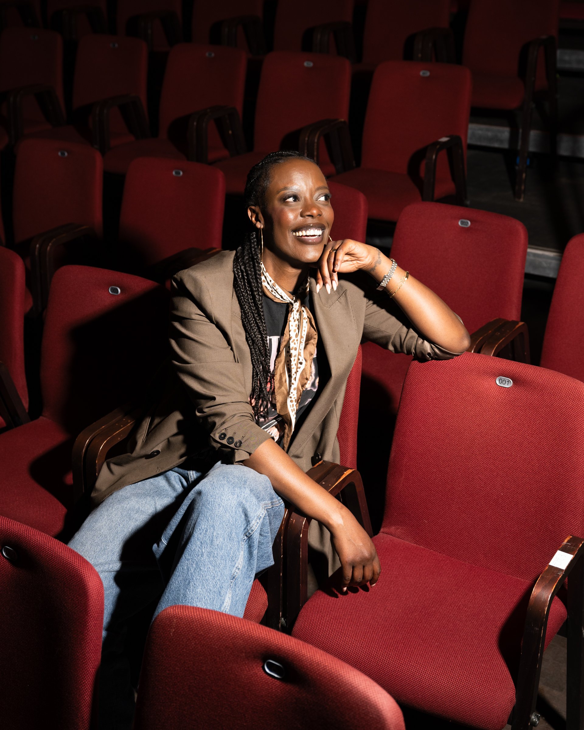 Kultur- und Eventfotografie lit.pop.cologne: Anna Dushime sitzt in einem leeren Theater mit roten Sitzen während einer Literaturveranstaltung und Portraitaufnahme