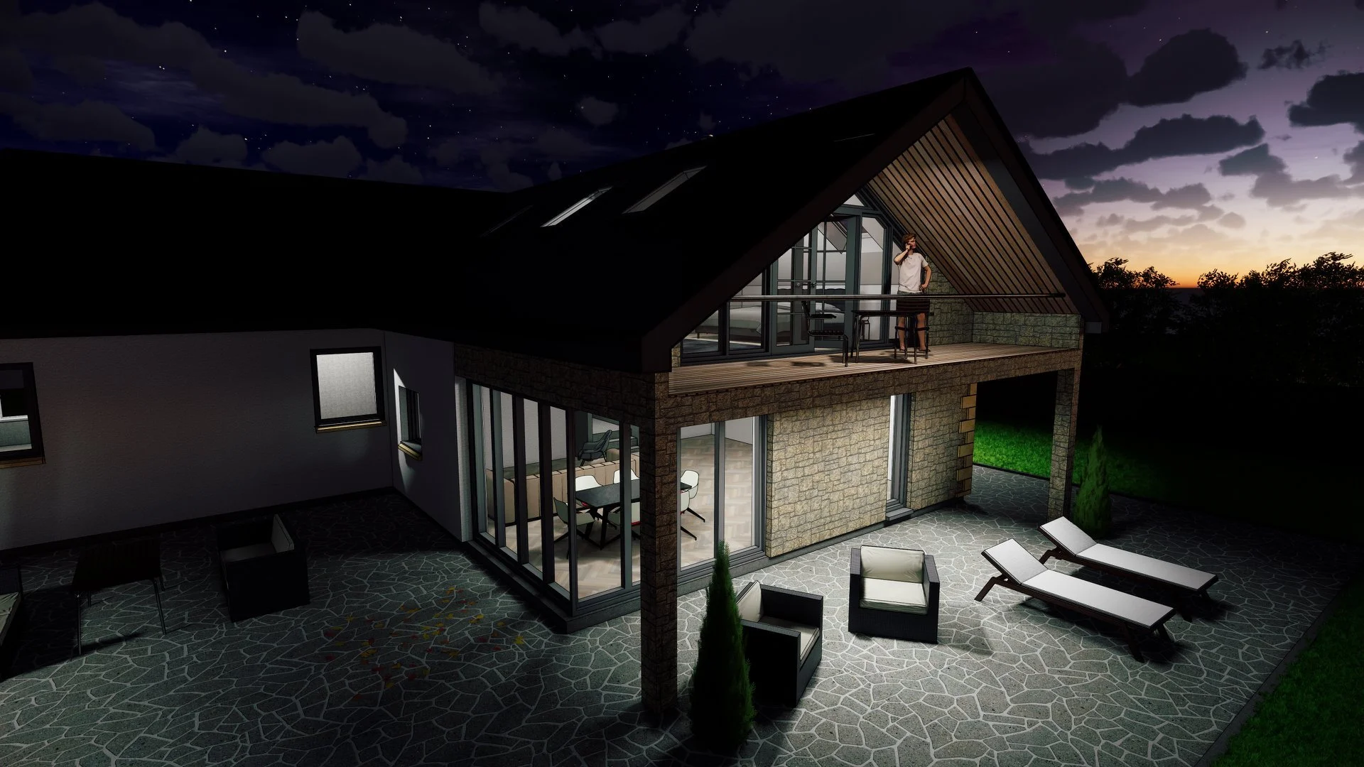 Night view of a modern house with a glass-enclosed dining area on the ground floor and a spacious balcony on the upper level. The house features stone and glass exterior walls, a sloped roof, and outdoor patio furniture including lounge chairs and seating. A man stands on the balcony, looking out at the sunset sky.