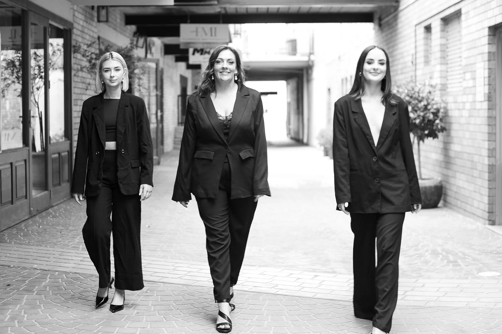 Three beauticians in business suits walking on a brick sidewalk in an urban outdoor setting. Beauty therapy and makeup in Mudgee