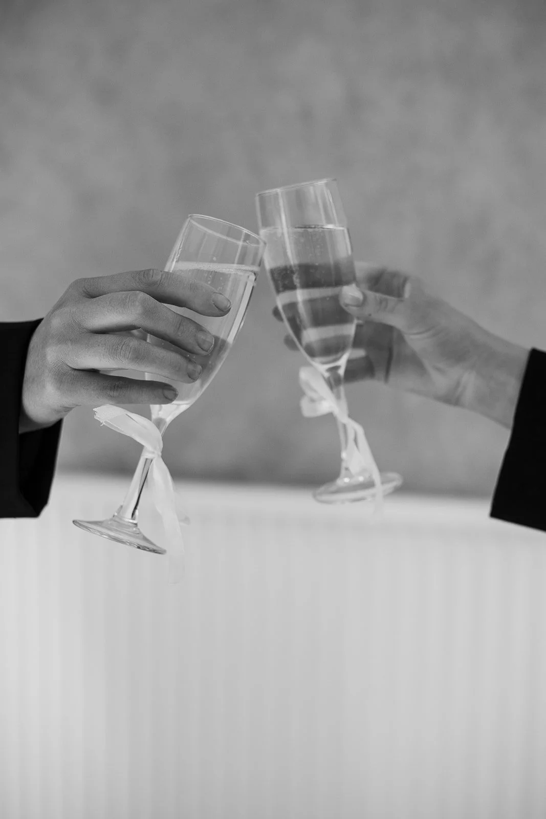 Two people in dark suits clinking glasses filled with a sparkling beverage, likely champagne, in a toast. Make up hens parties, kids parties and workshops