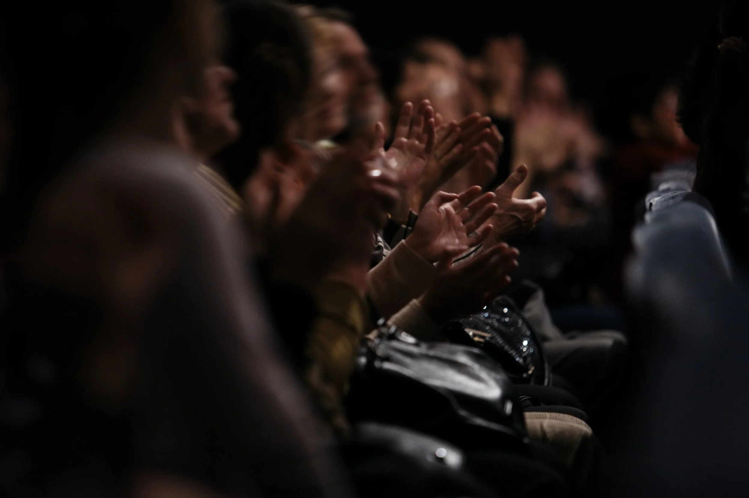 Audience clapping in a dark auditorium.