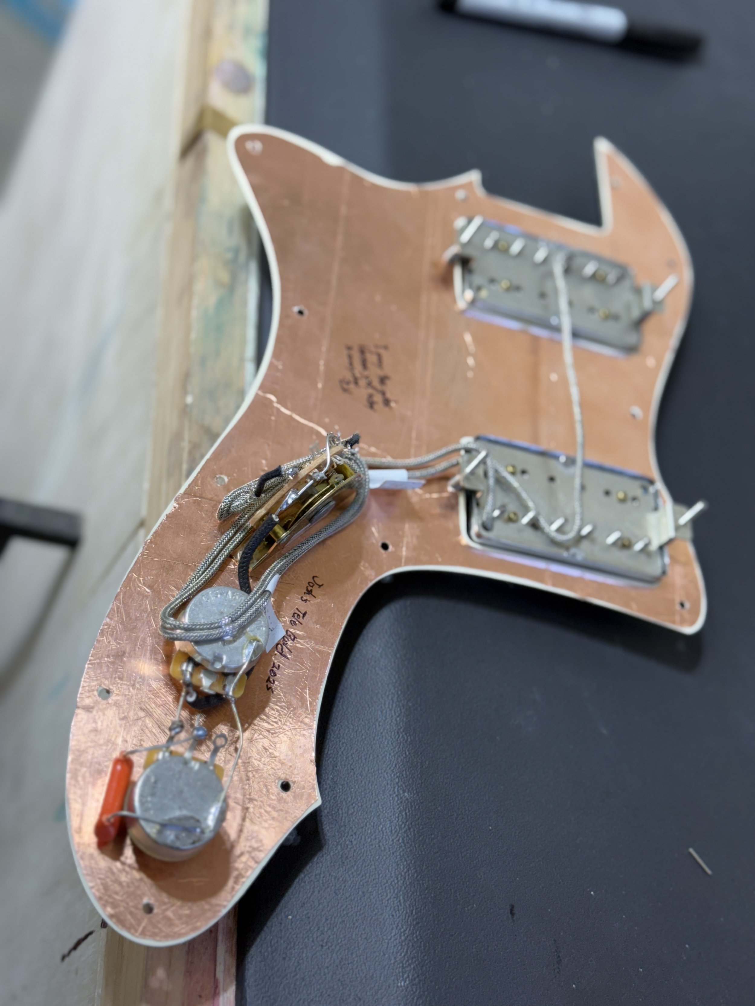 Part of an electric guitar's pickguard with electronic components and wiring attached, resting on a work surface.