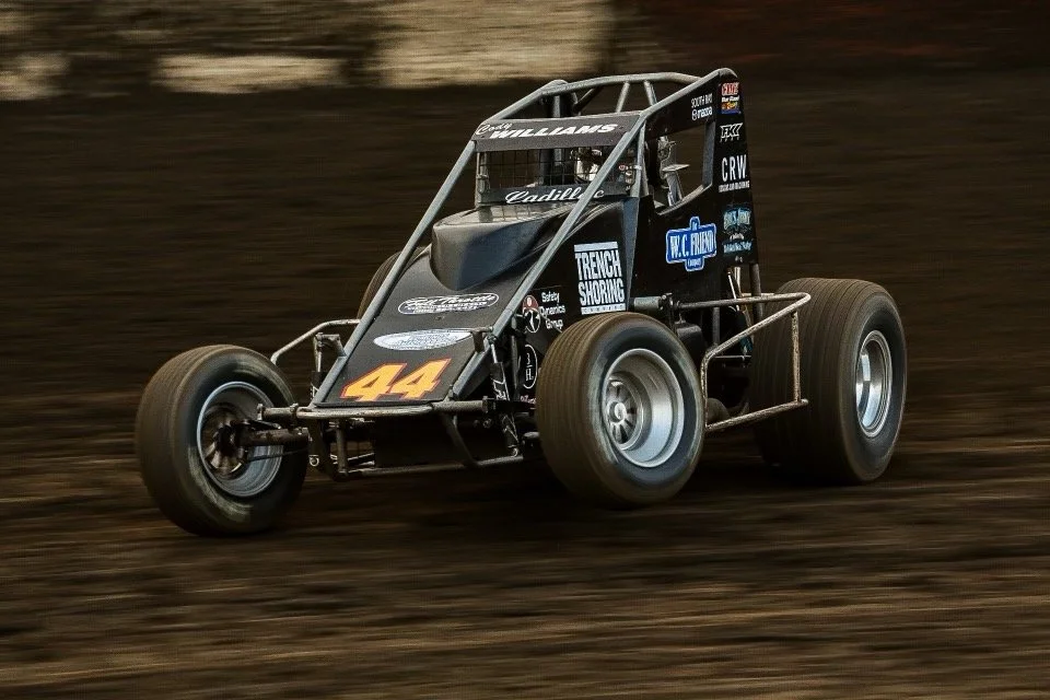 A black sprint car with the number 44 racing on a dirt track.
