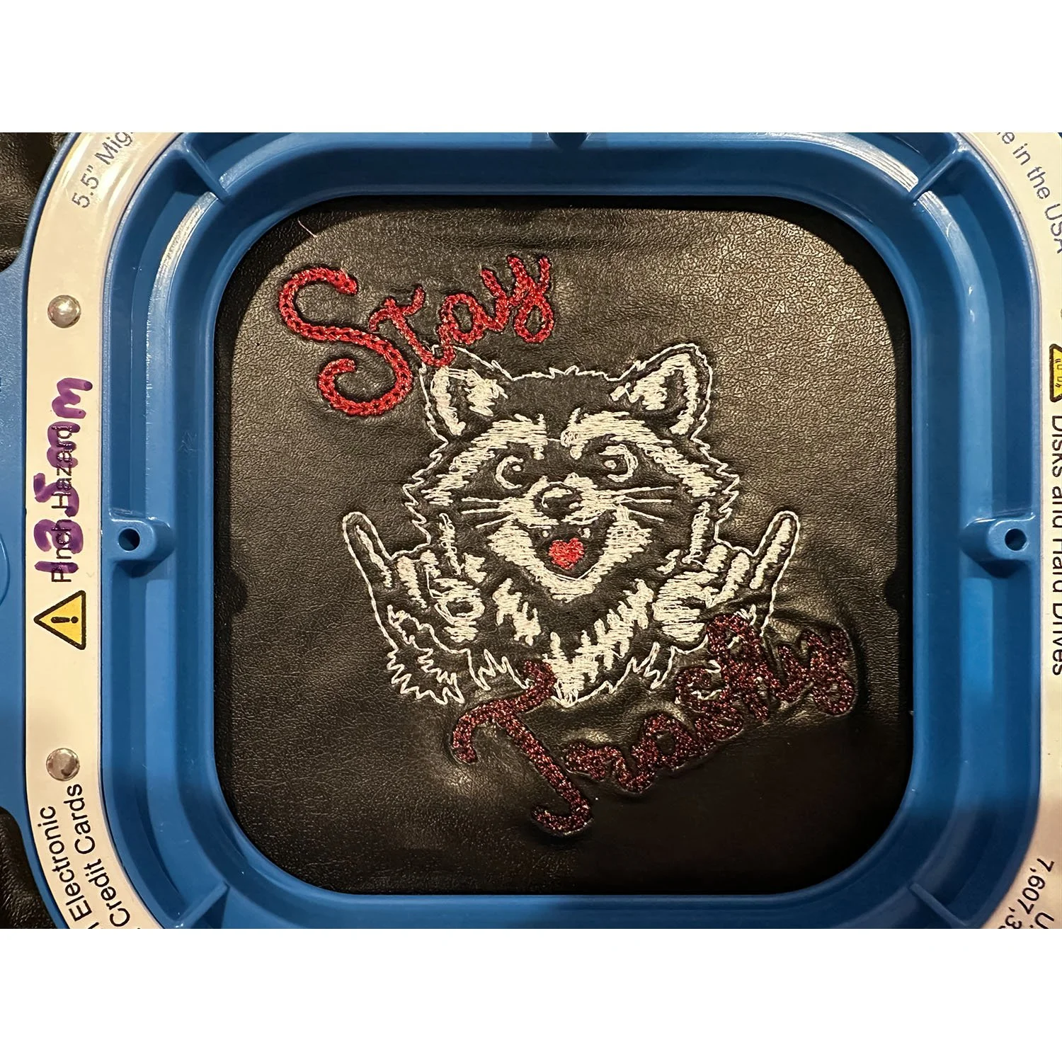 Raccoon throwing the rock and roll sign with "Stay" embroidered in red above and "Trashy" embroidered in red below