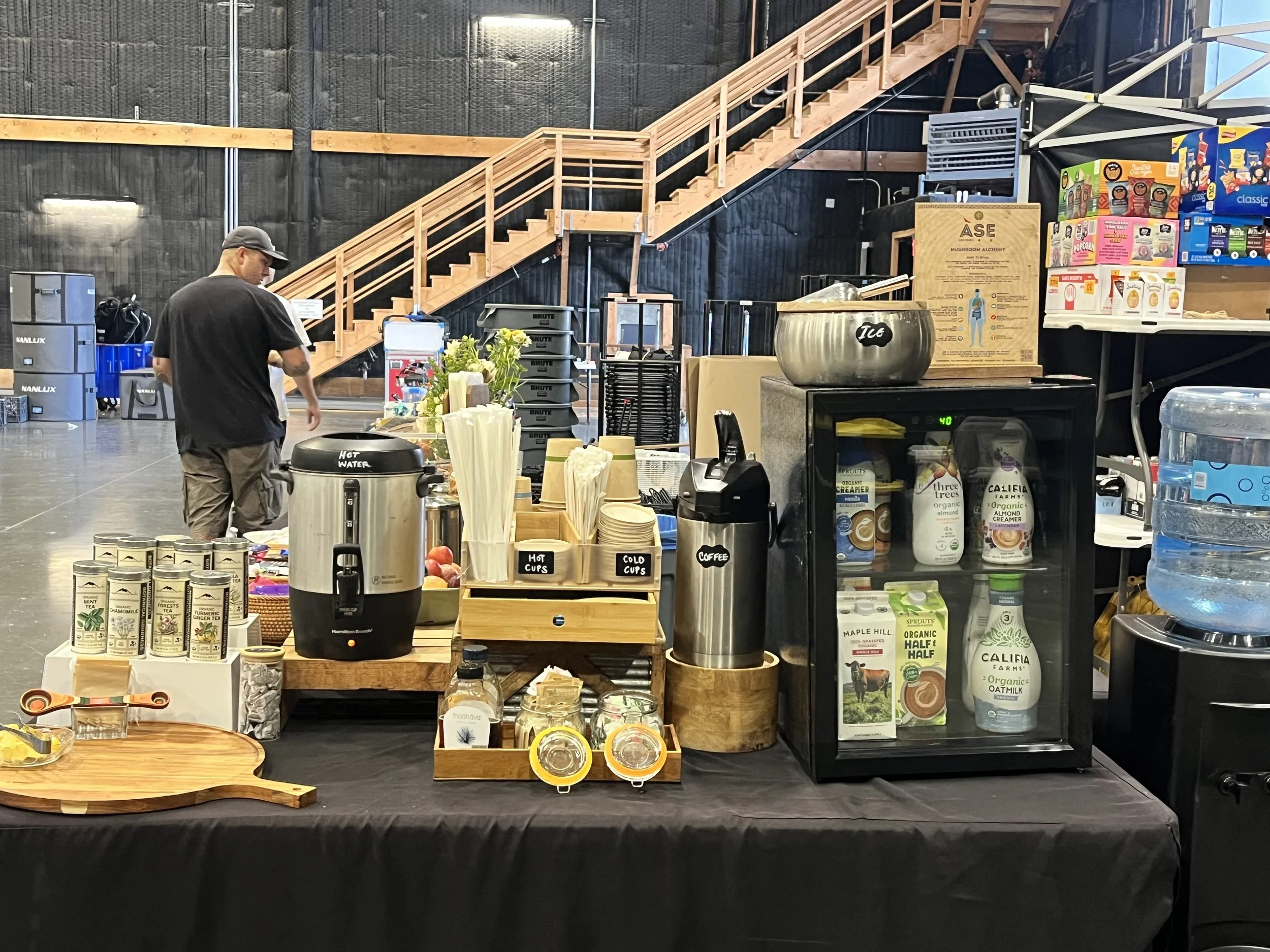 Indoor of a Sound Stage with various packaged products, including teas, drinks, and snacks, on tables and shelves in the foreground, a man browsing and working behind the counter.