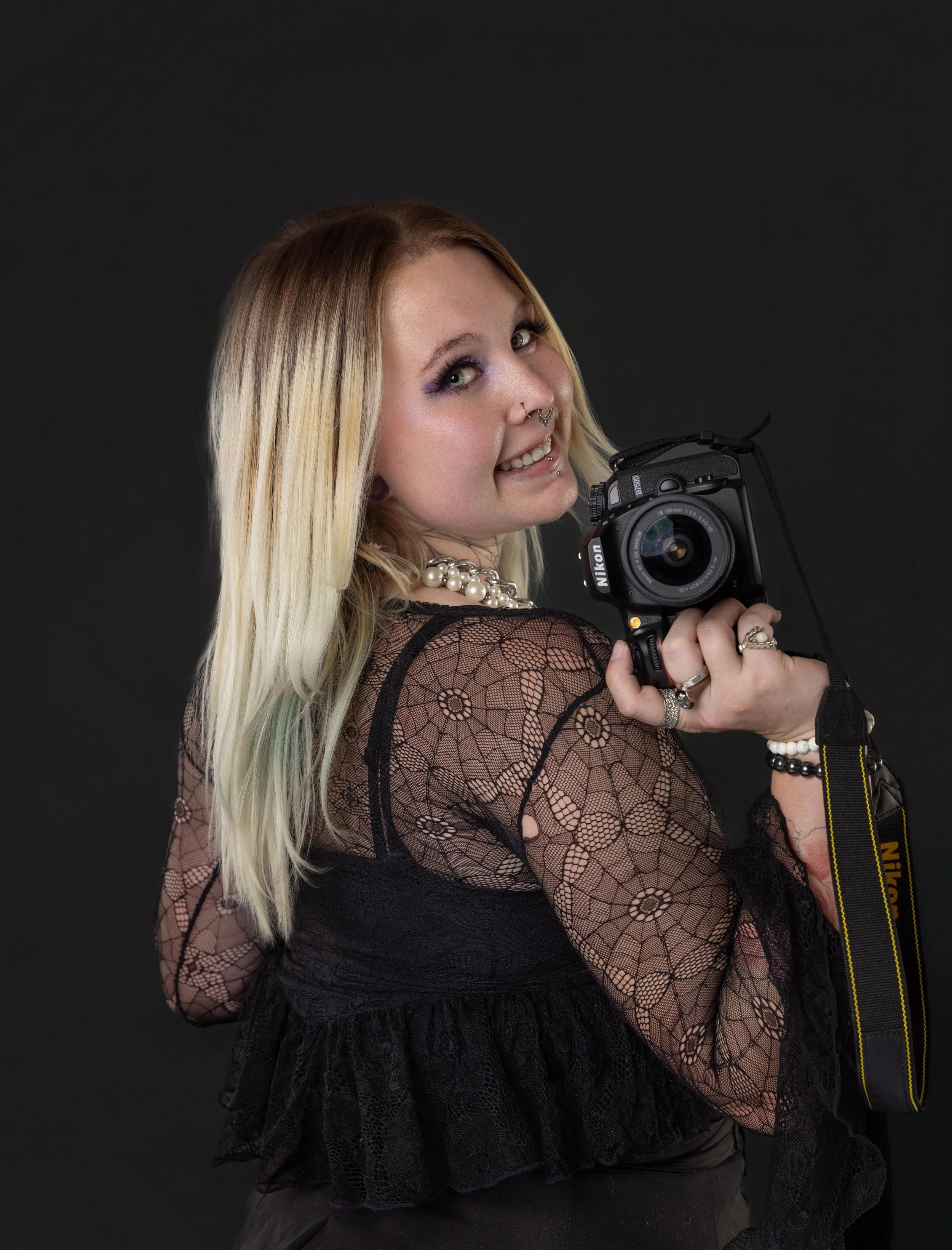 Portrait of Angel, photographer and Aesthetic Collective team member, holding a camera against a dark studio backdrop in Grand Junction, Colorado.