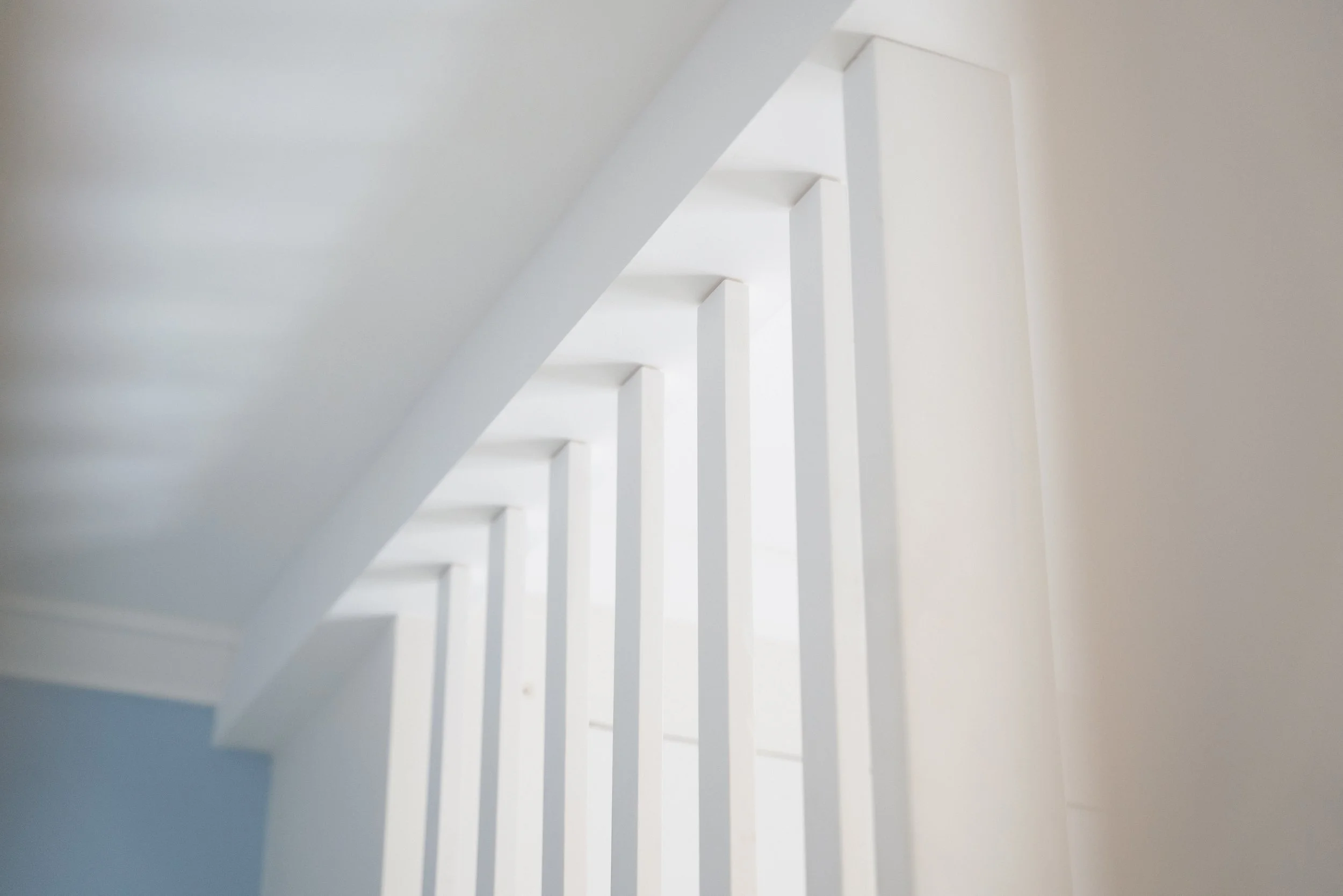 Close-up of a white staircase railing with vertical bars and a sloped ceiling, in a well-lit room.
