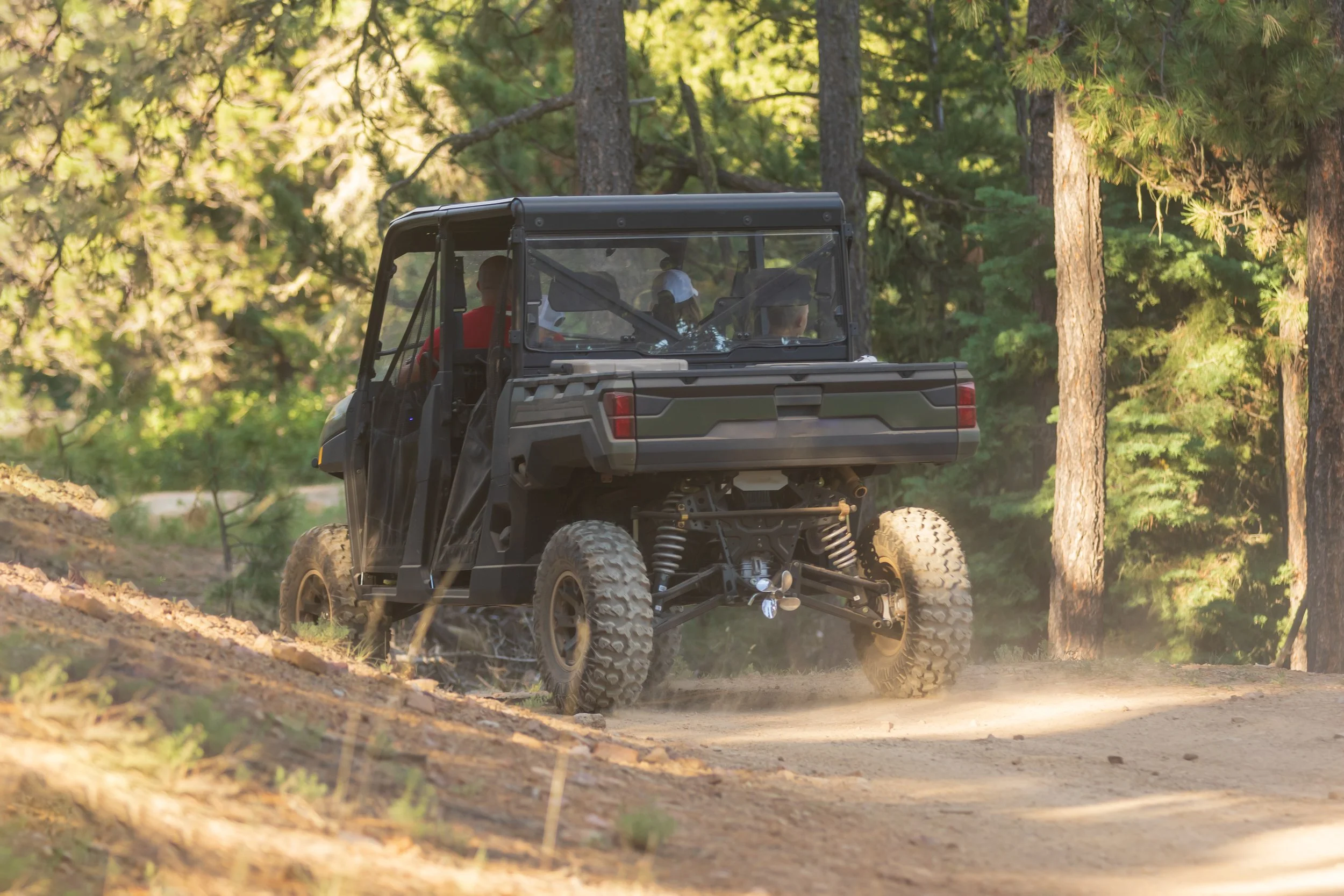 A black off-road utility vehicle driving on a dirt trail through a forest with green trees.