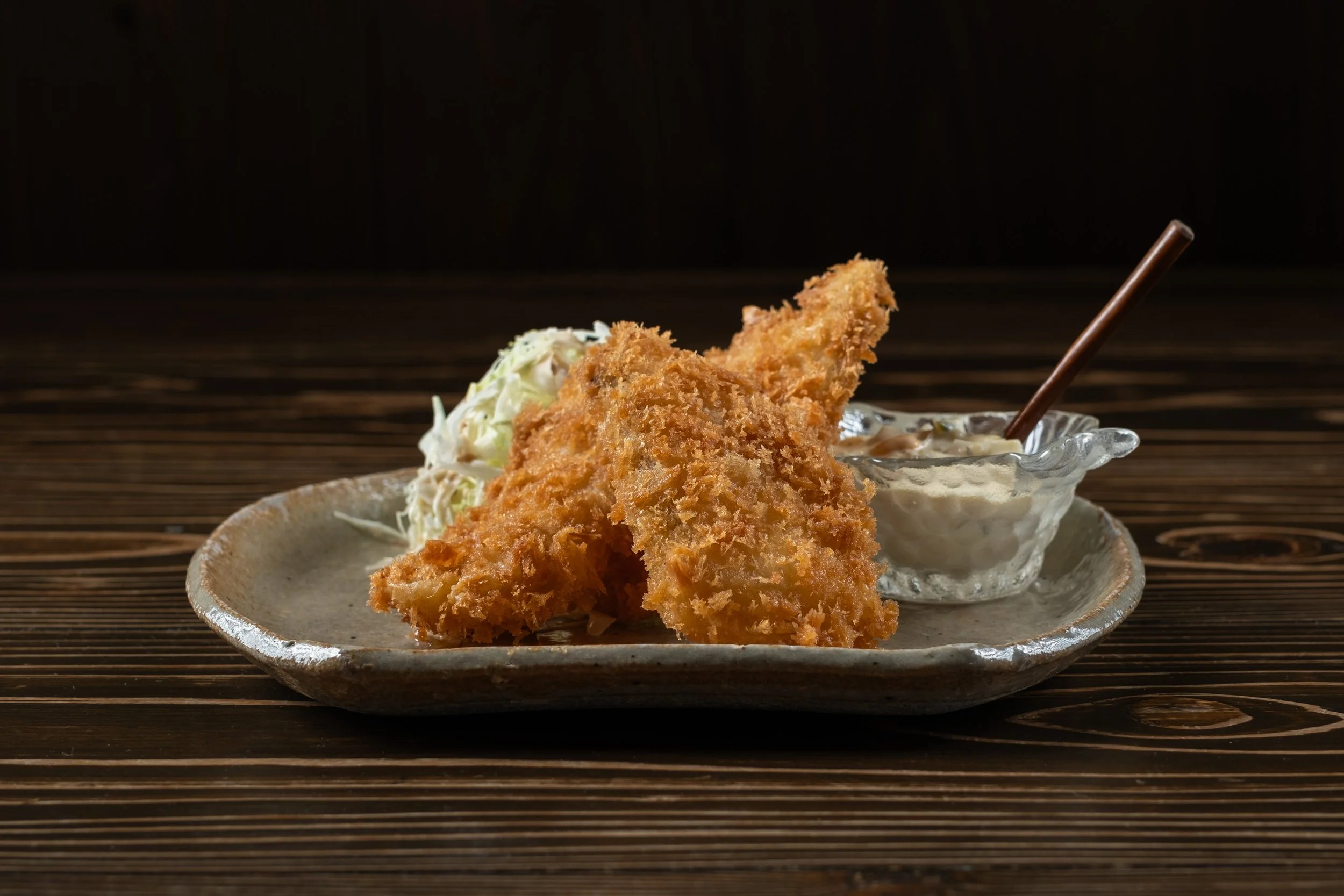 揚げたてのフライとキャベツのサラダ、タルタルソースの付け合わせが載った陶器の皿