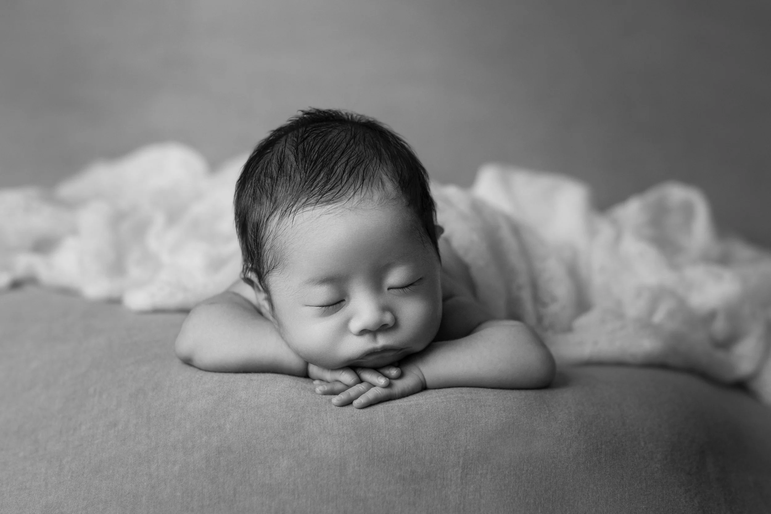 眠っている赤ちゃんのクローズアップ。両腕を折りたたんで枕にして顔を乗せ、背景にふわふわしたブランケットがある。