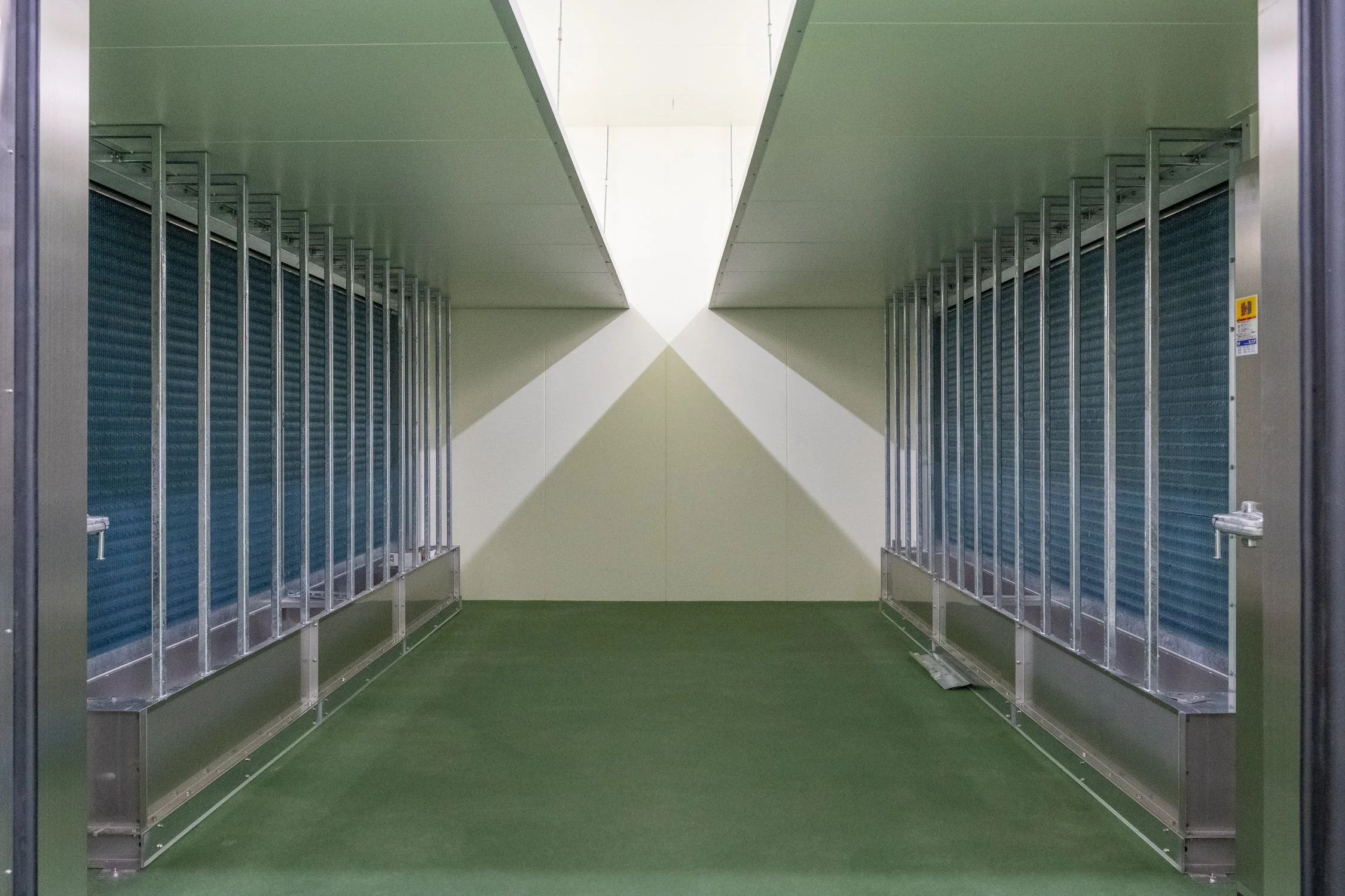 空の荷物棚が並ぶ空洞の通路。緑色の床と白い壁が見える。