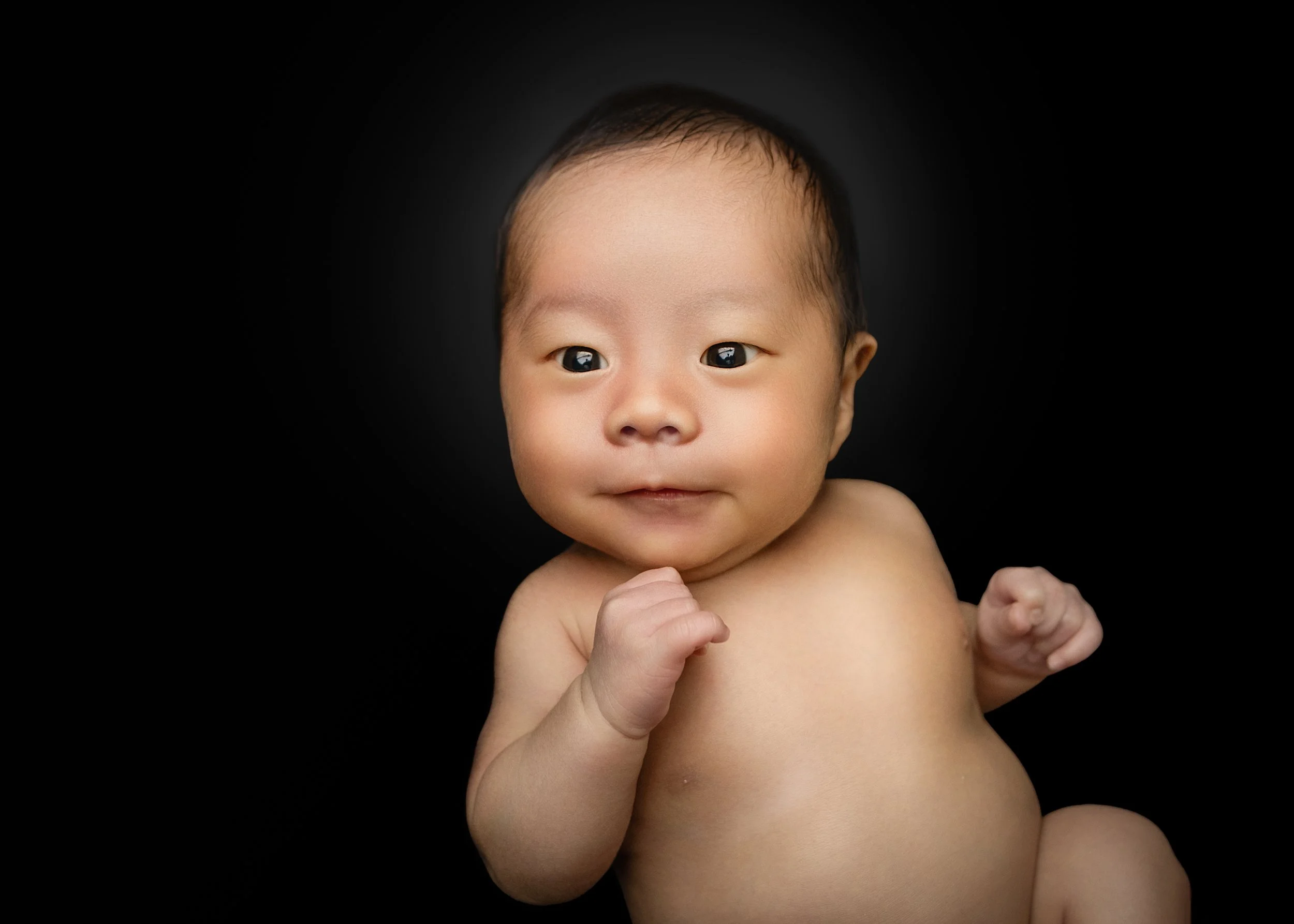 黒い背景の前で微笑む赤ちゃんの上半身。