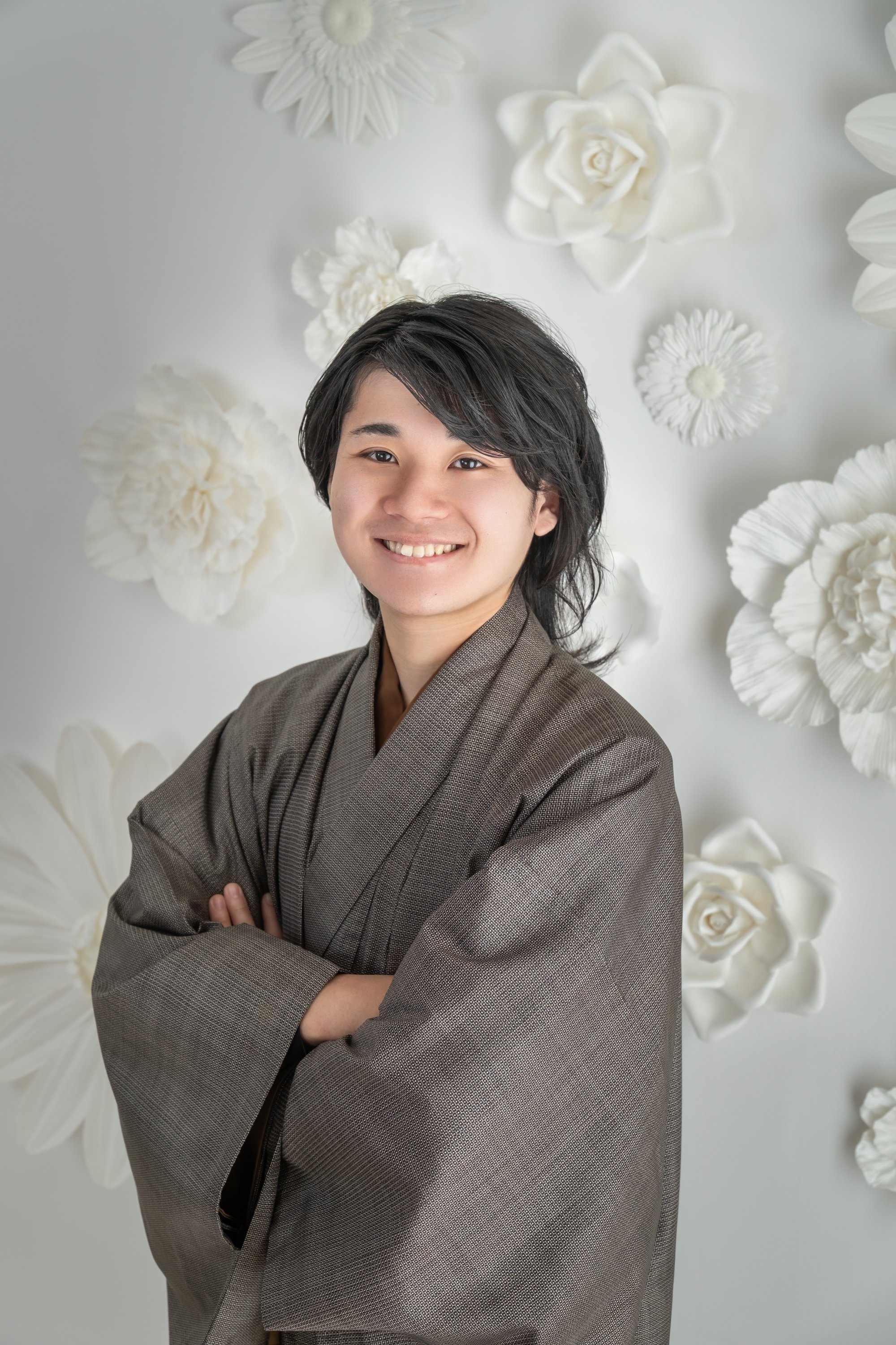 和服を着た若い男性の肖像写真。背景には白い花の装飾がある。