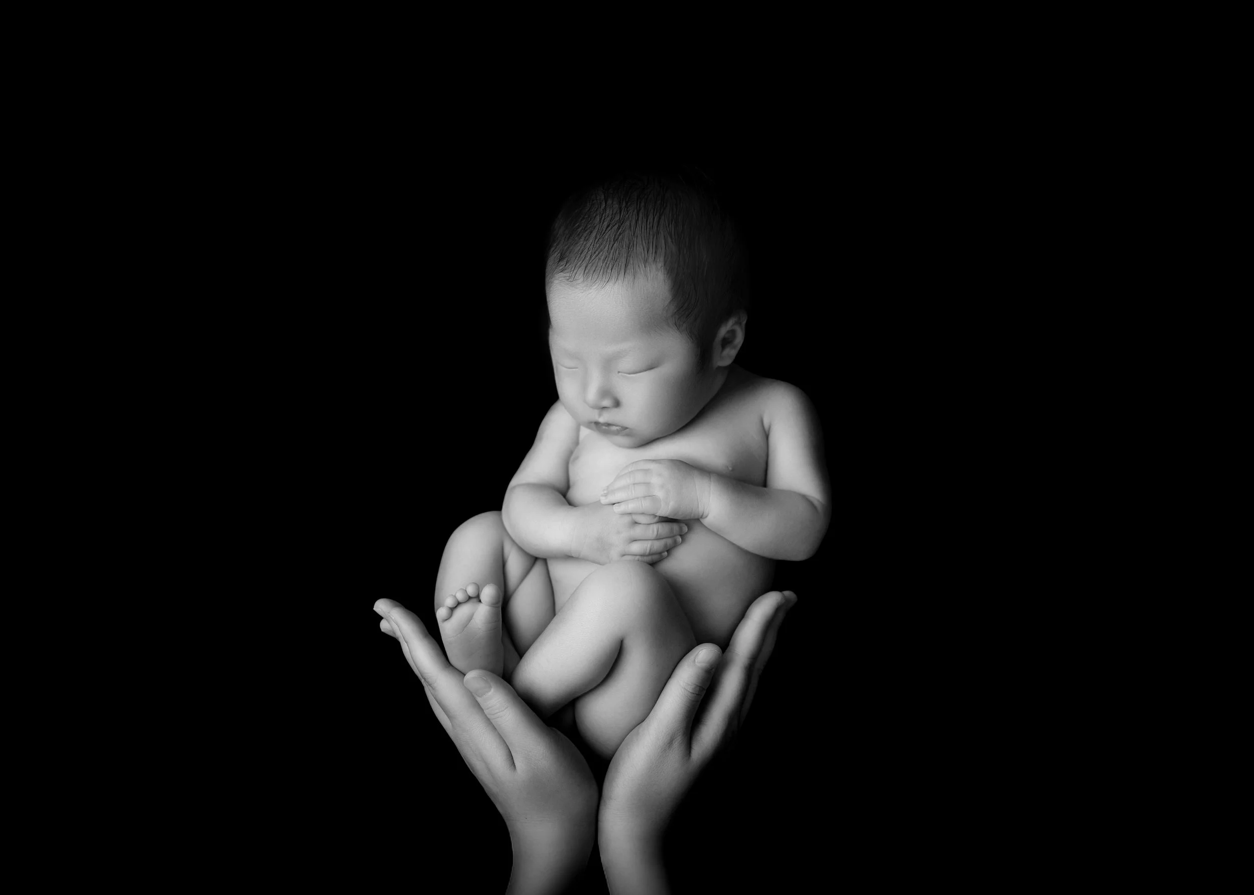 黒背景に抱きかかえられる赤ちゃんの白黒写真