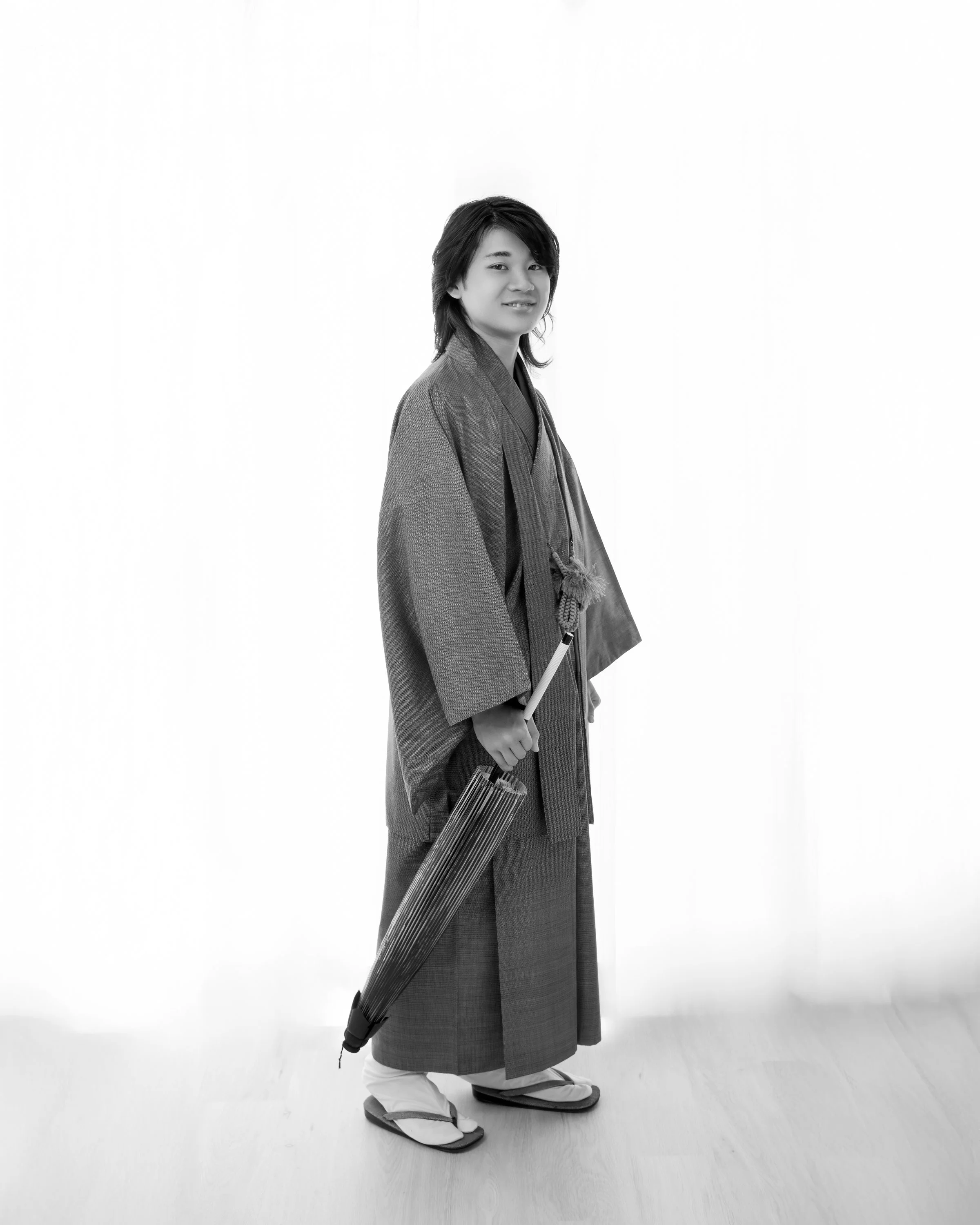 伝統的な日本の着物を着た男性が長傘を持ち、木製の床の上に立っている