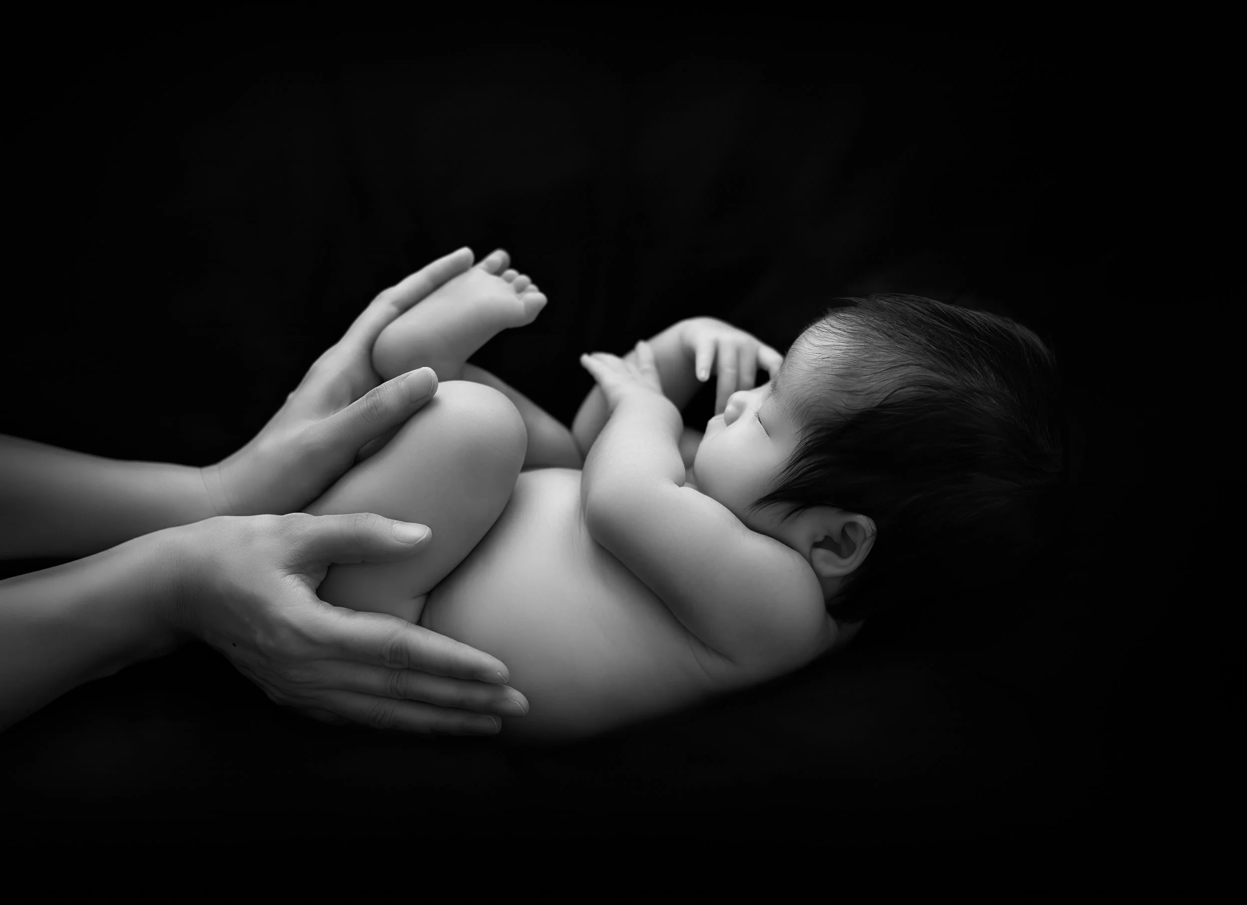 赤ちゃんを優しく抱きしめるように、母親の手が触れているシーンの白黒写真