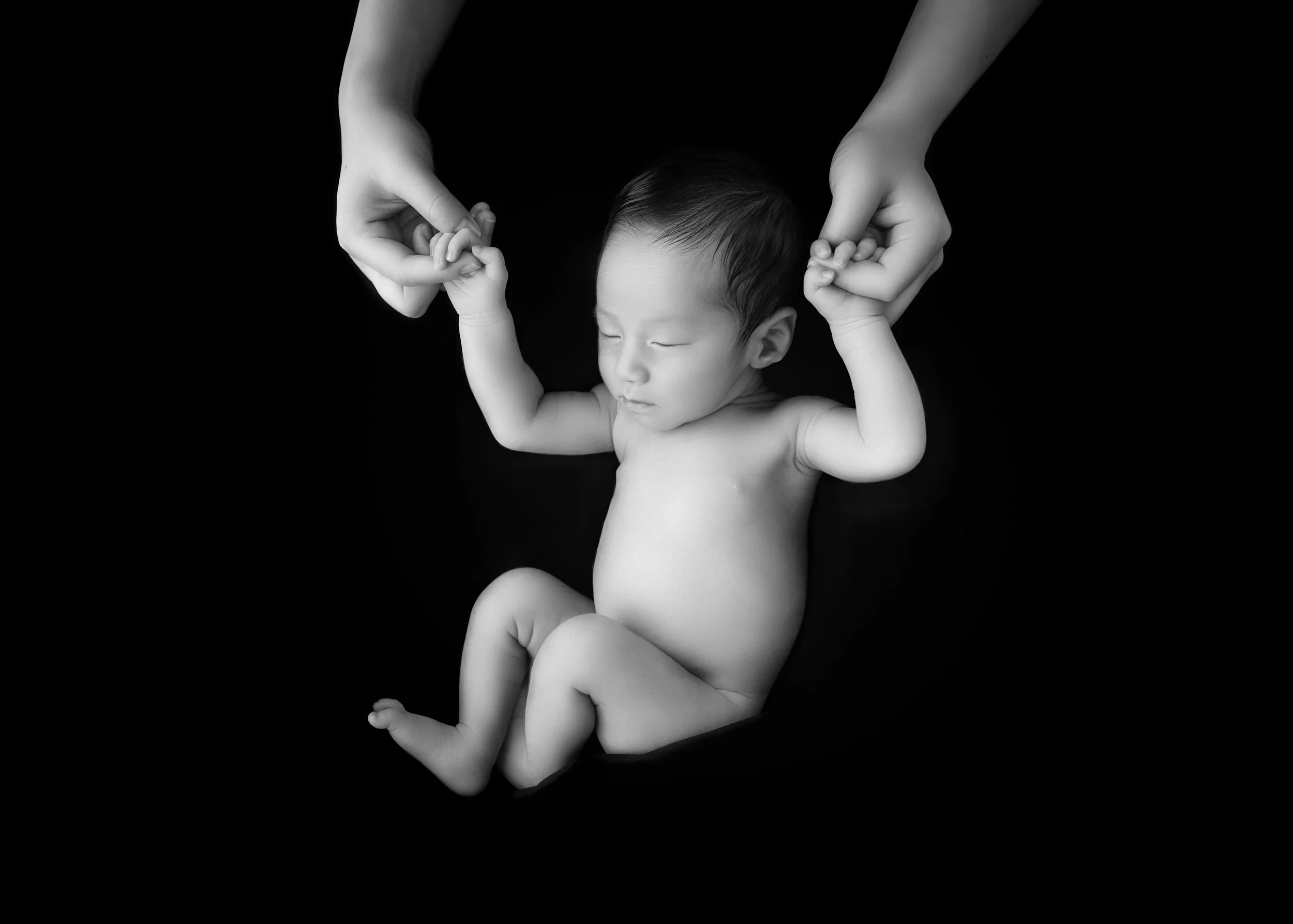黒い背景に寝ている赤ちゃんを両手で握る大人の手。