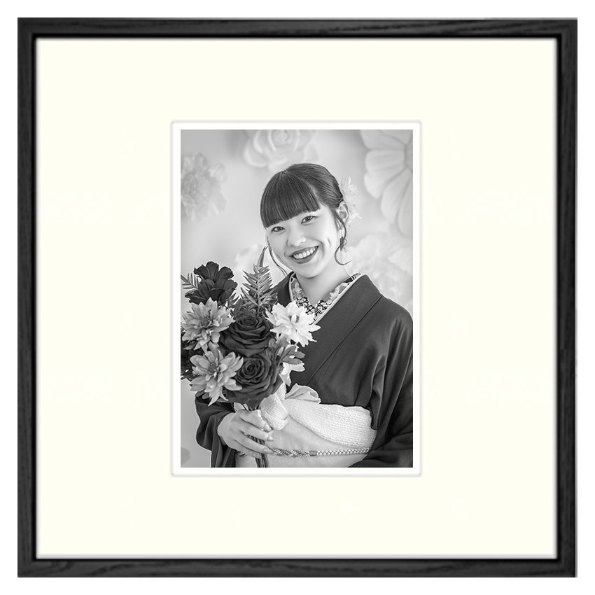 笑顔の女性が花束を持っている白黒の写真。背景は花の模様が描かれている。フレームに収められている。